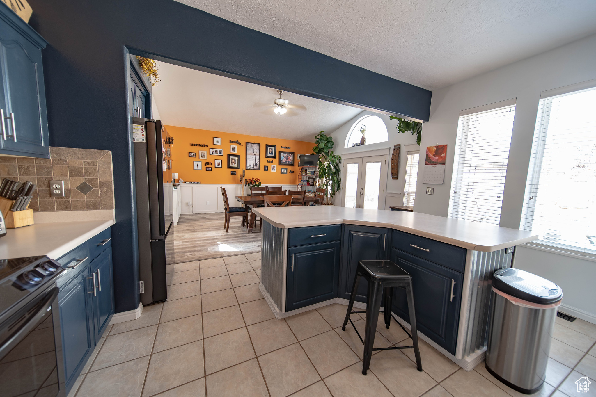 Kitchen with blue cabinets, a kitchen breakfast bar, range with electric cooktop, black fridge, and kitchen peninsula