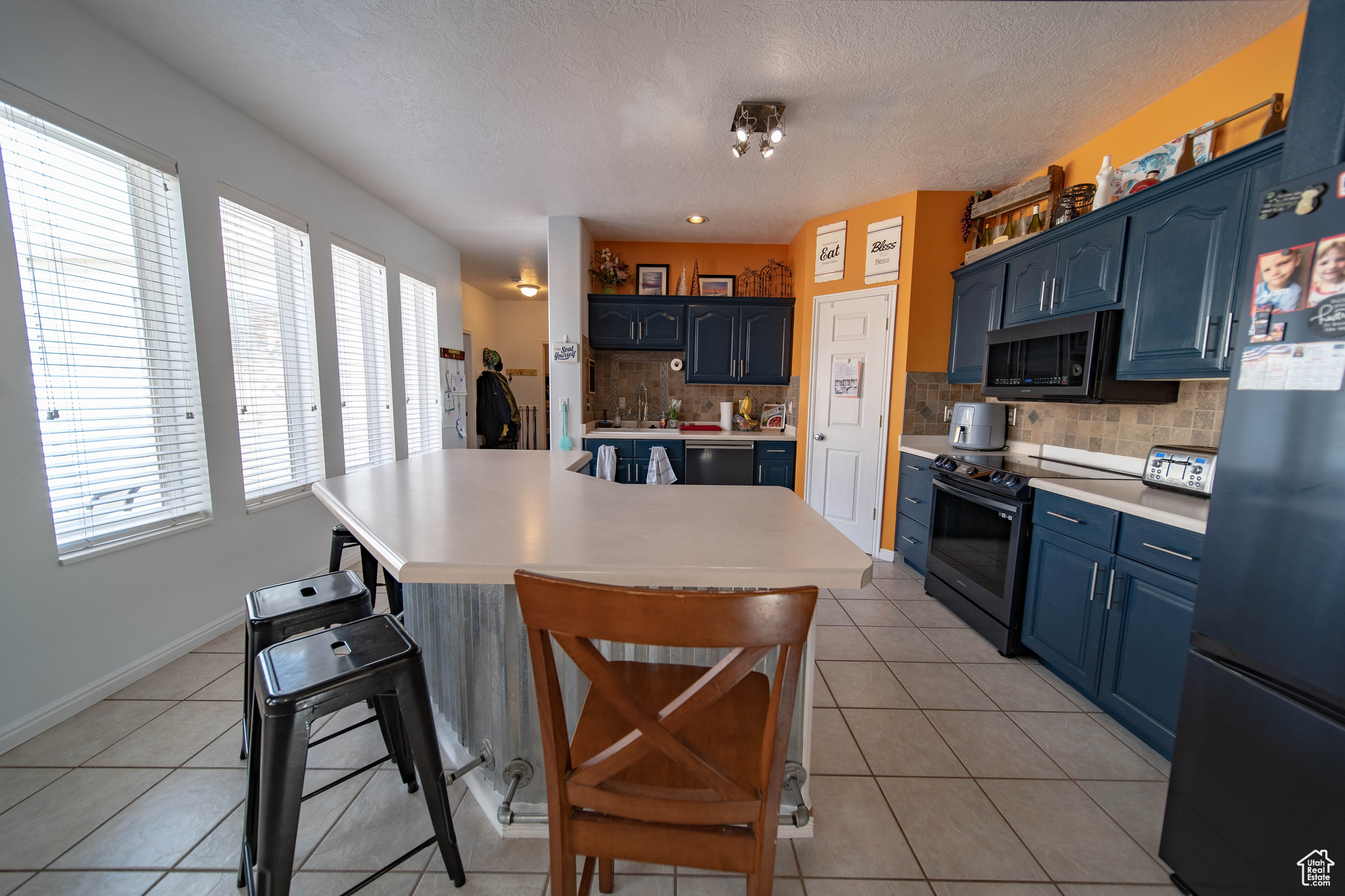Kitchen with range with electric cooktop, black refrigerator, a breakfast bar area, and light tile patterned floors