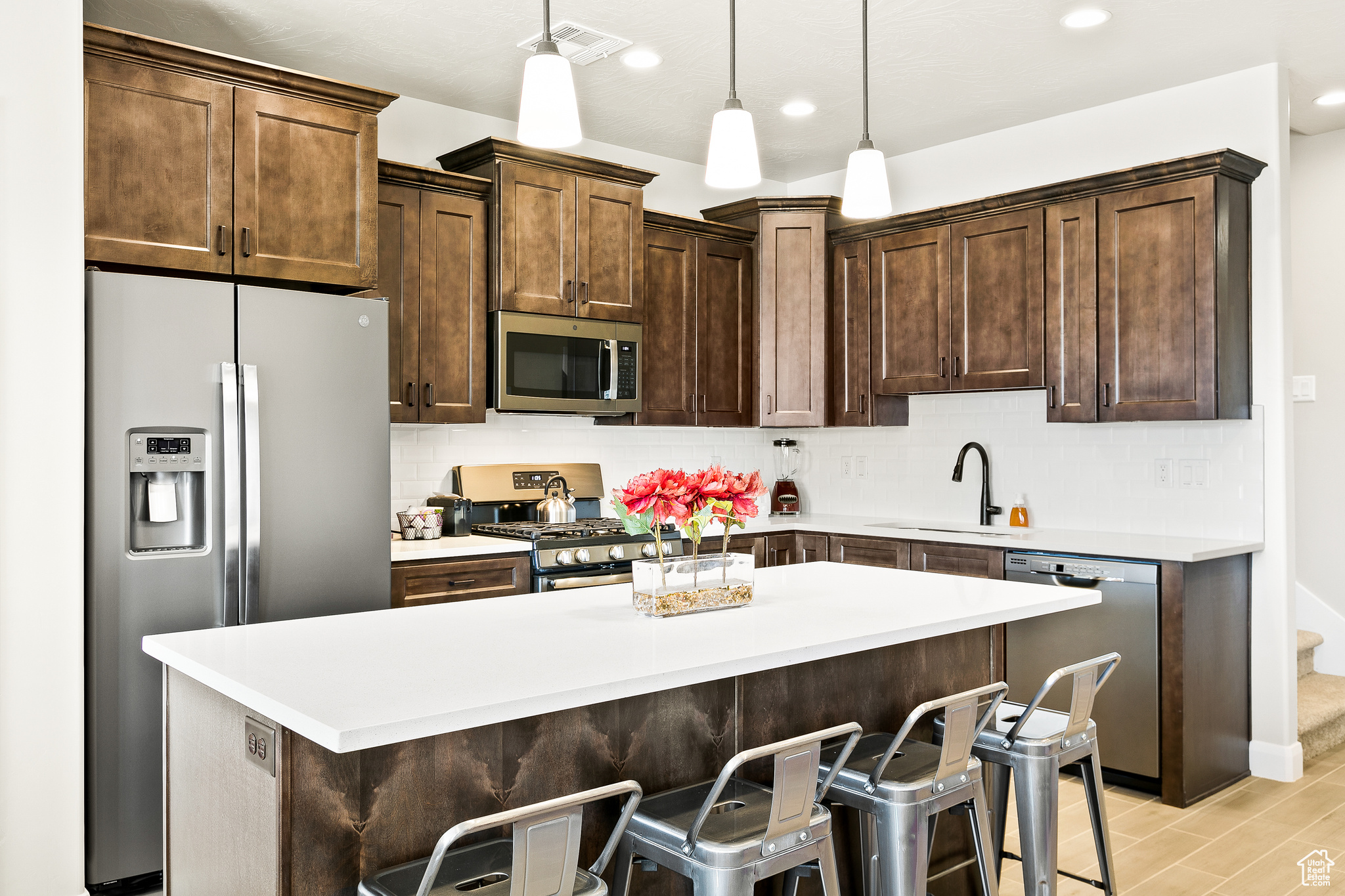 Kitchen featuring sink, backsplash, pendant lighting, stainless steel appliances, and a breakfast bar area