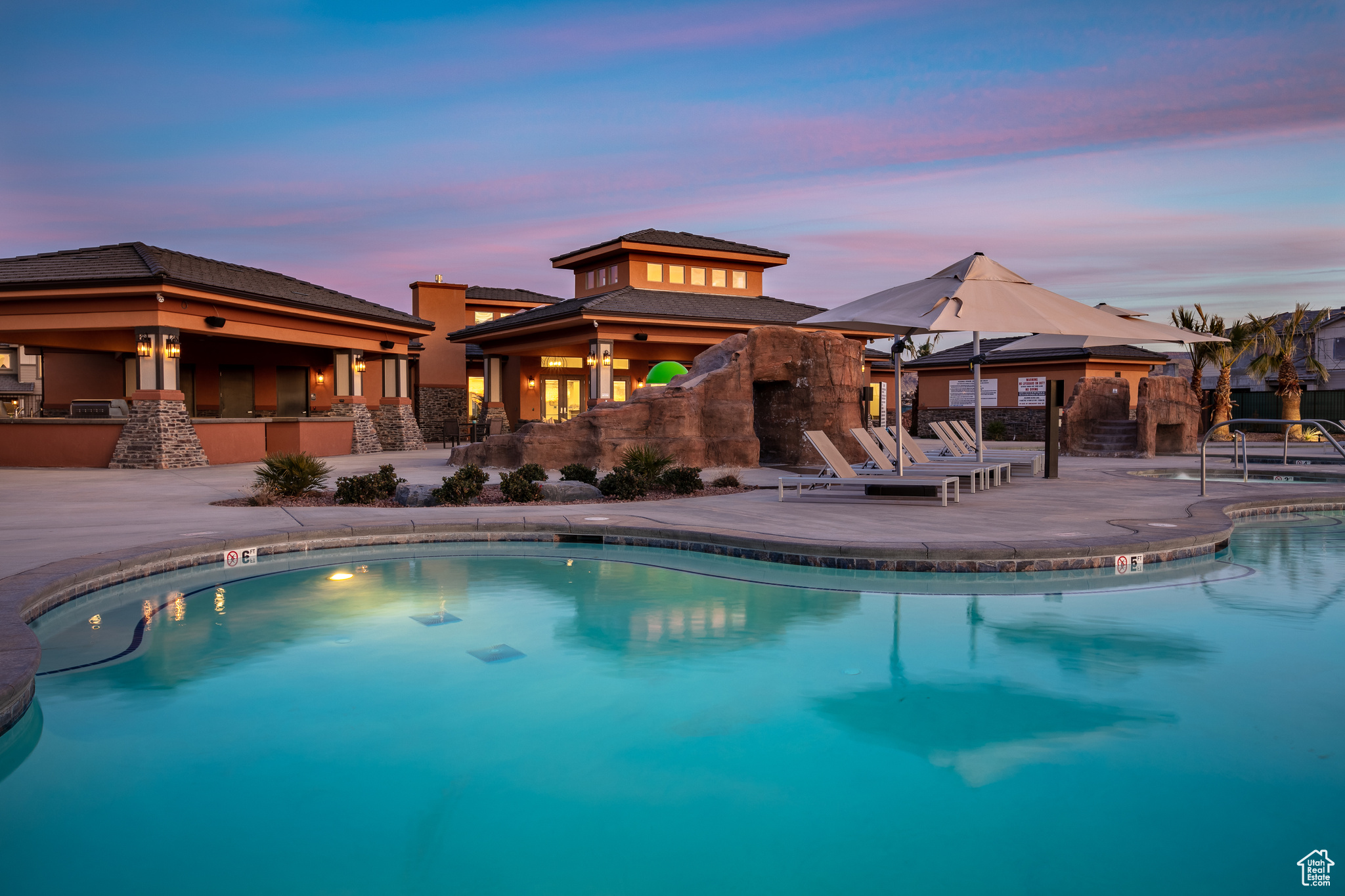 Pool at dusk featuring exterior bar, an outdoor kitchen, and a patio
