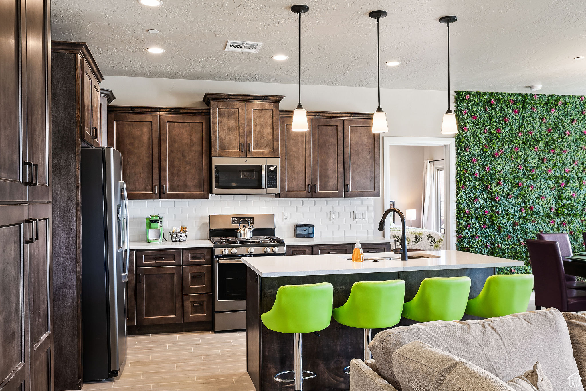 Kitchen with stainless steel appliances, decorative backsplash, pendant lighting, sink, and a kitchen island with sink