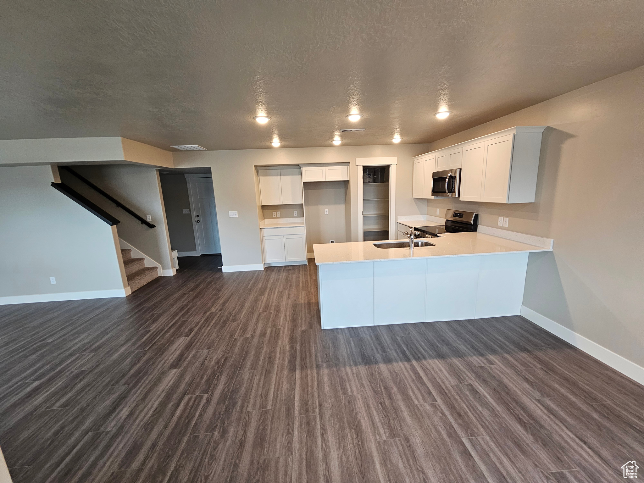 Kitchen with appliances with stainless steel finishes, dark wood-type flooring, white cabinets, sink, and kitchen peninsula