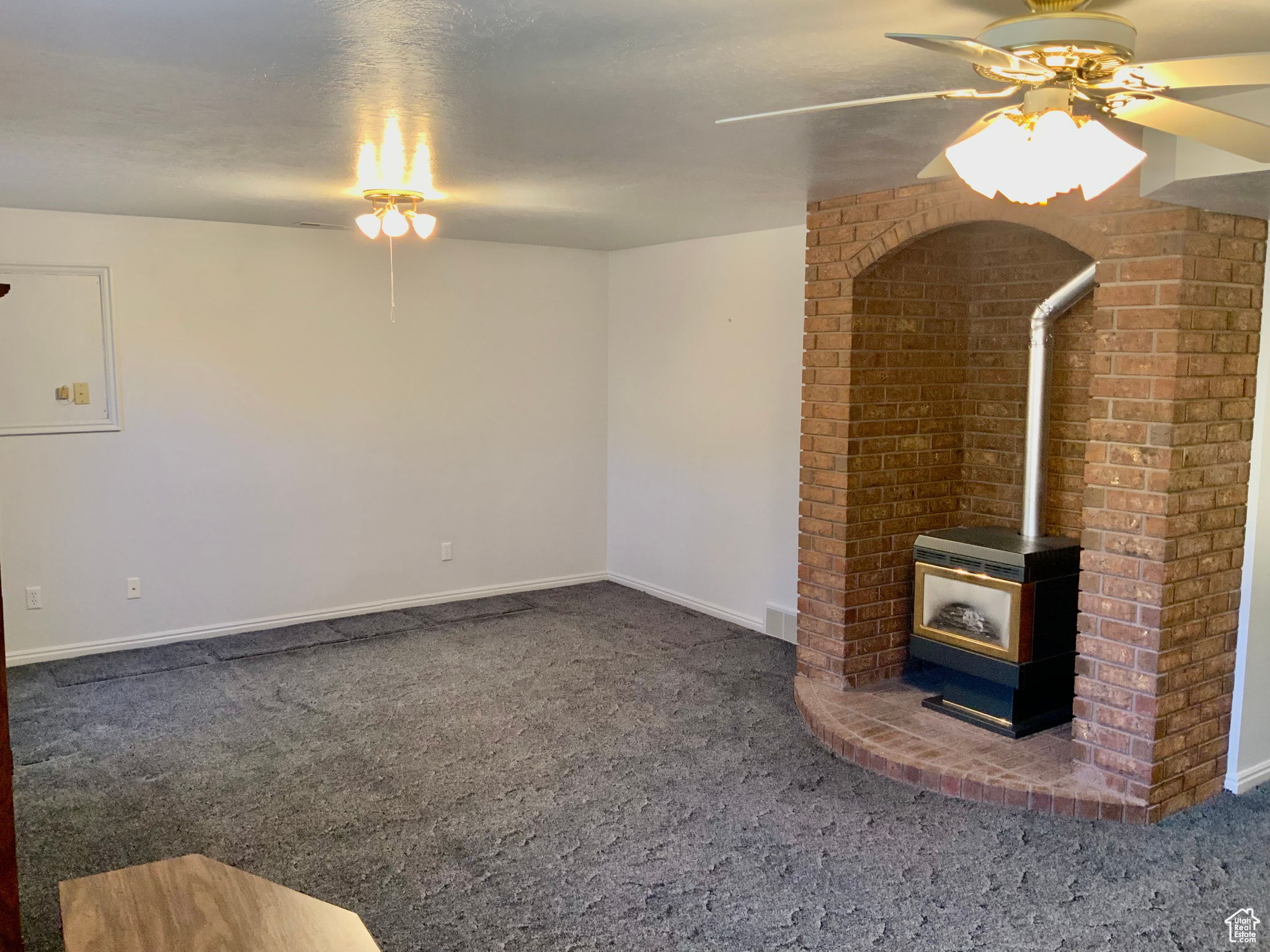 Unfurnished living room featuring a wood stove, ceiling fan, and dark colored carpet
