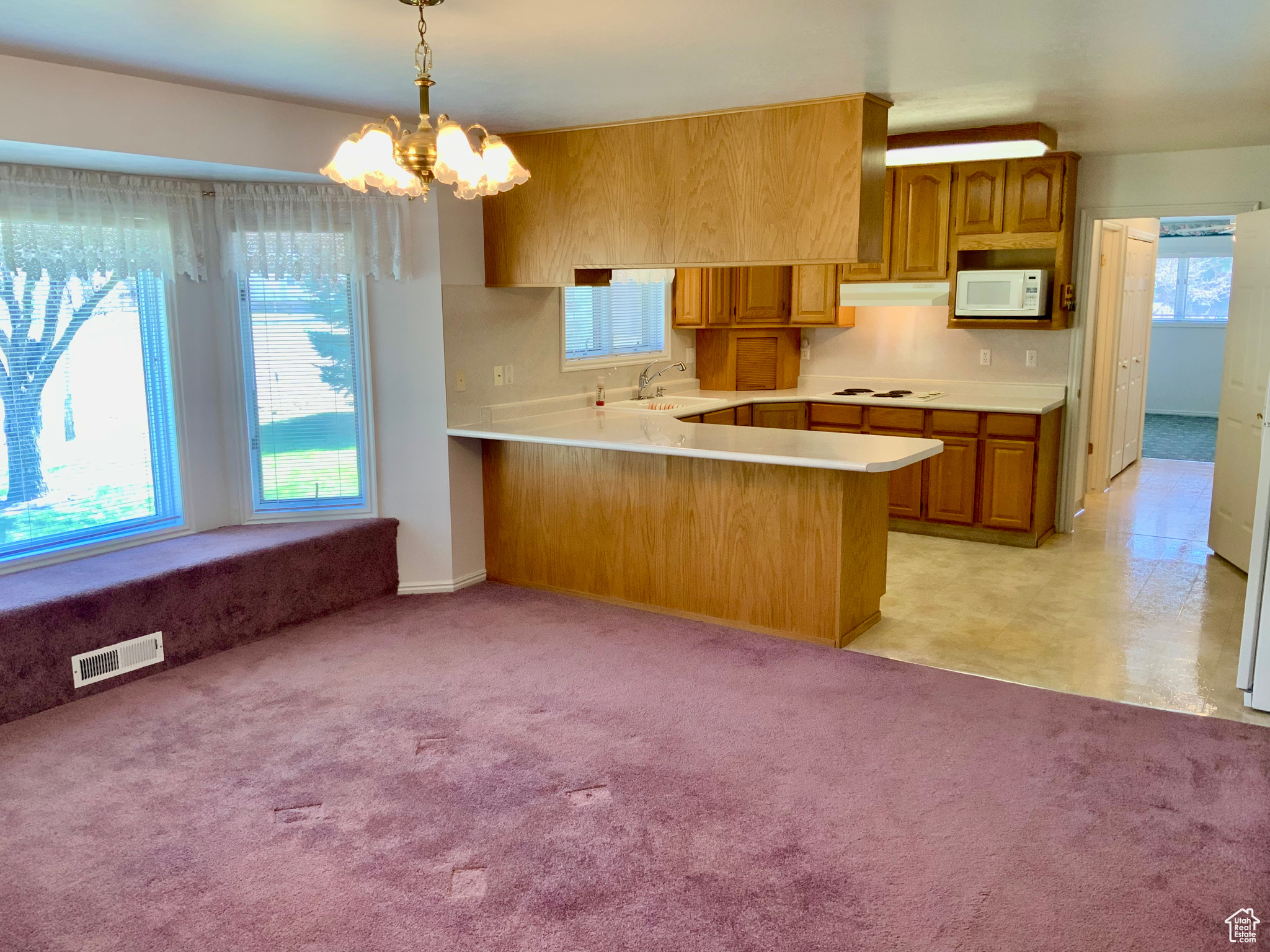 Kitchen with white appliances, a chandelier, kitchen peninsula, hanging light fixtures, and light carpet