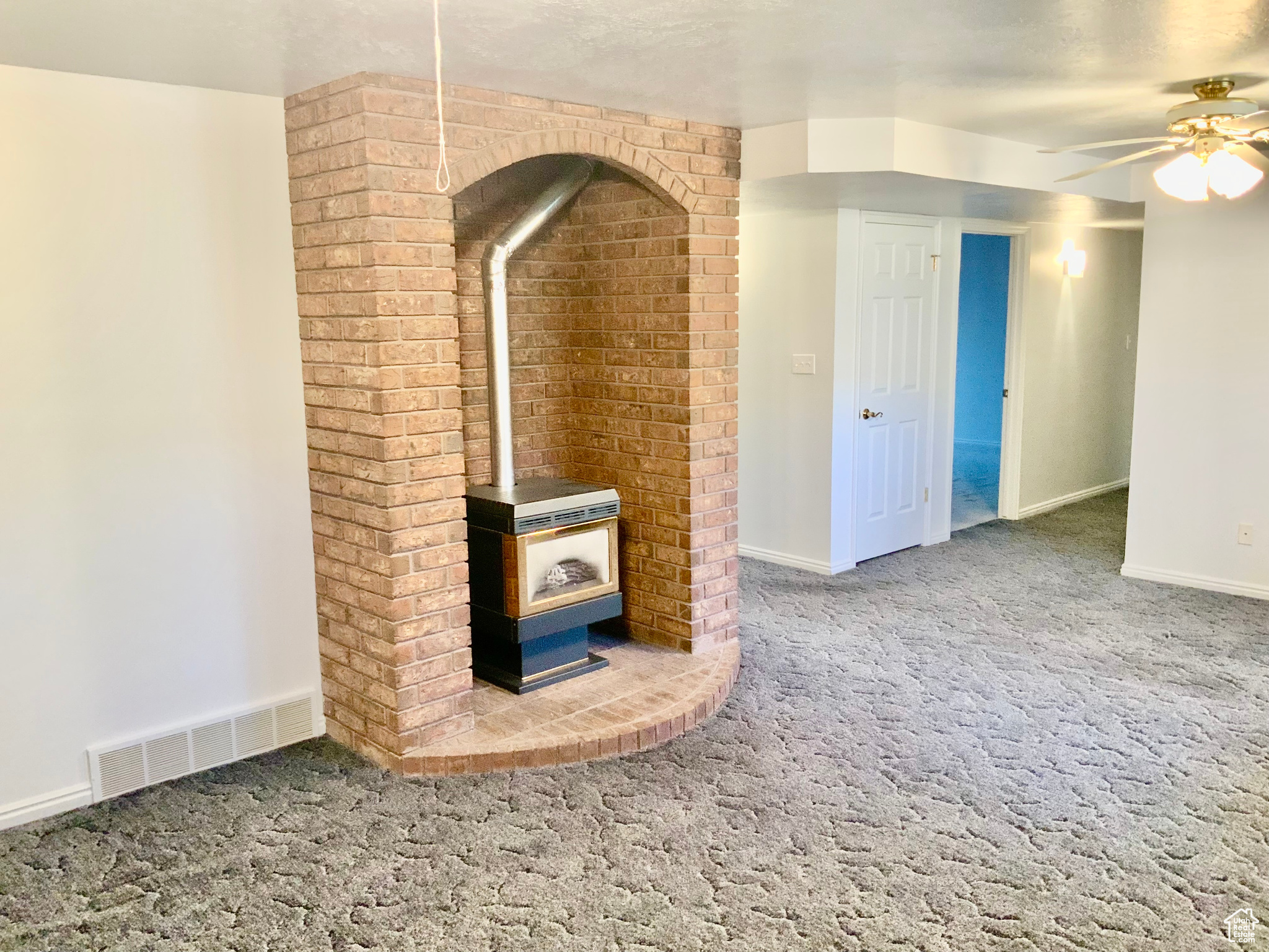 Unfurnished living room featuring carpet floors, a wood stove, and ceiling fan