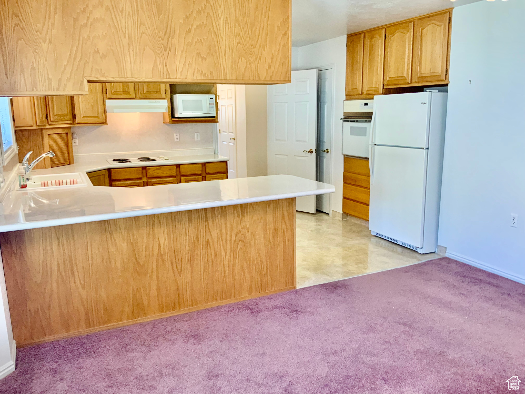 Kitchen with white appliances, light carpet, sink, and kitchen peninsula