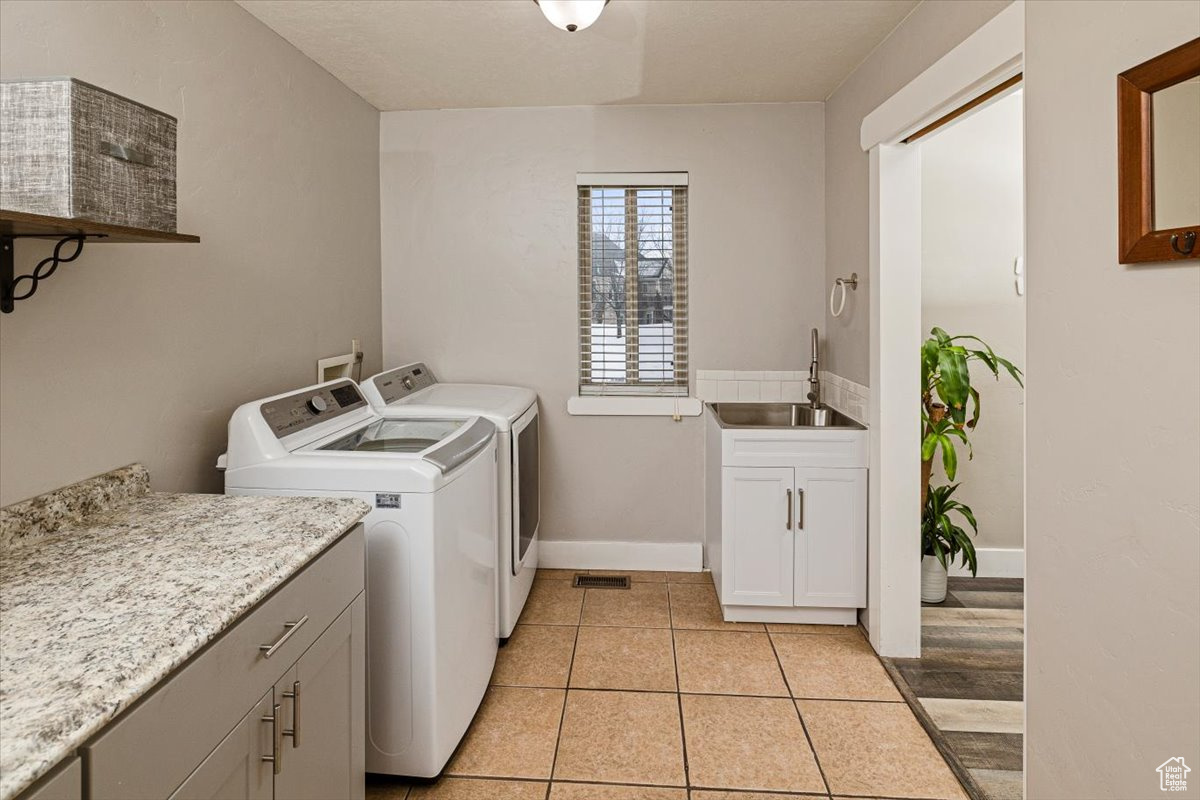 Washroom with sink, cabinets, light tile patterned flooring, and washing machine and clothes dryer