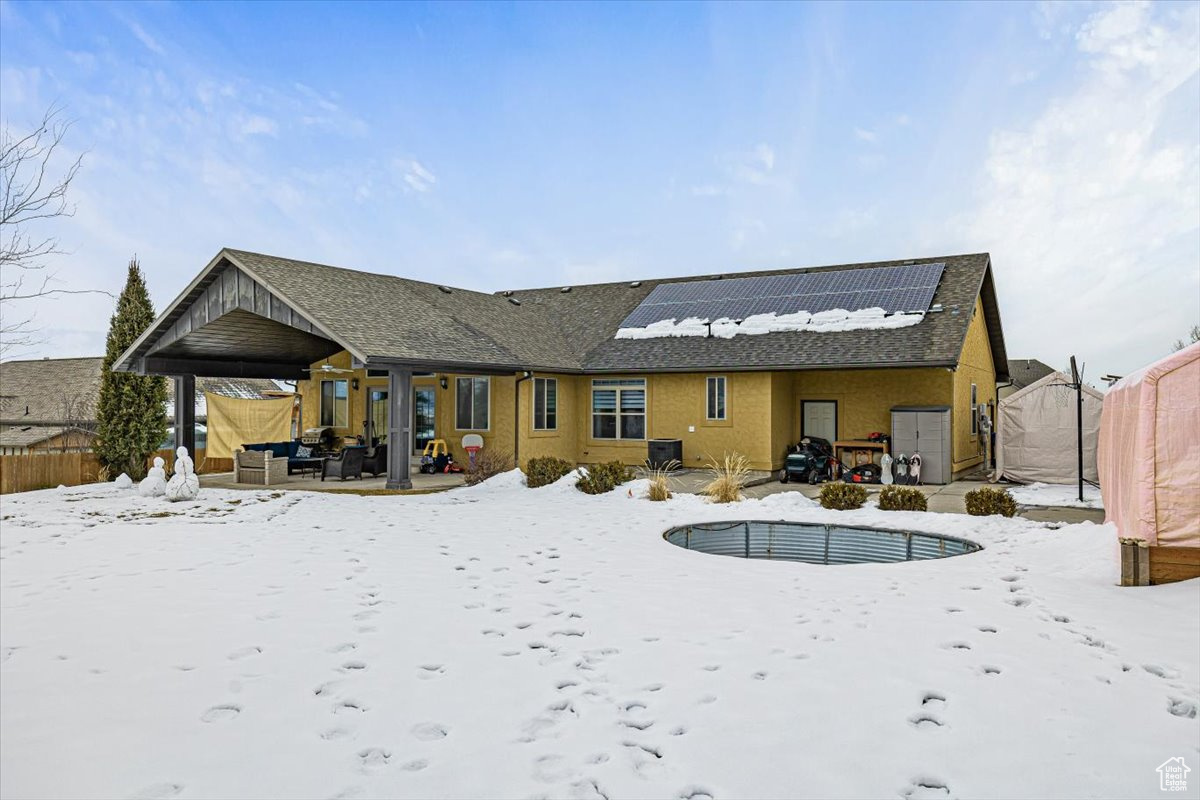 Snow covered house with solar panels, a patio, and a fenced backyard