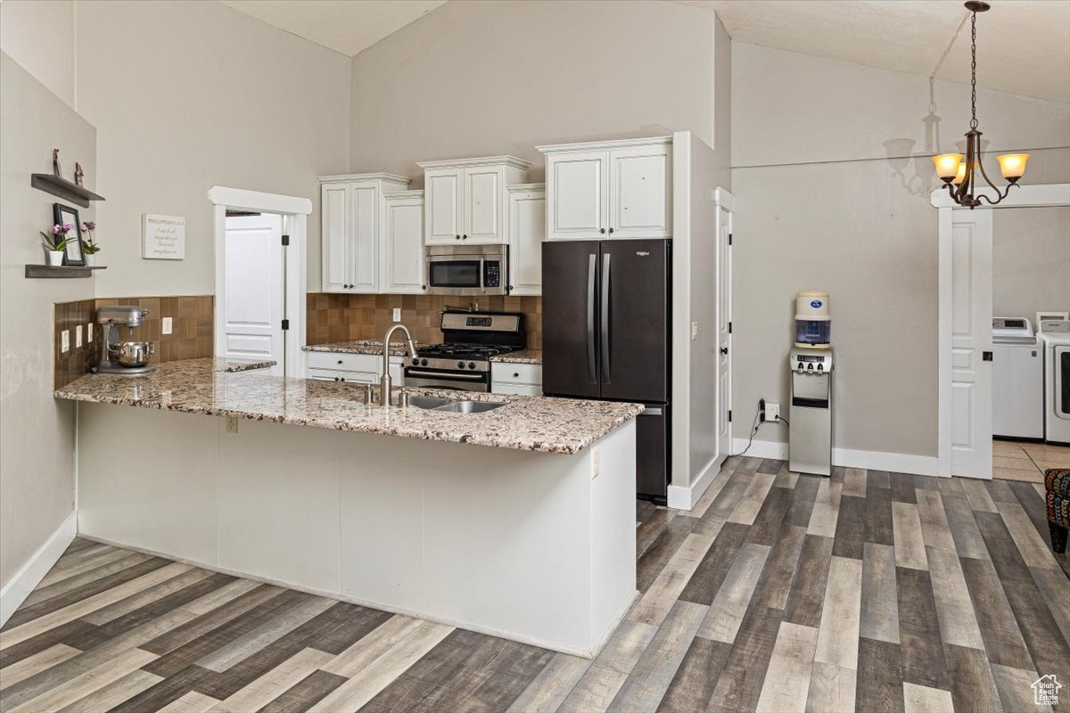 Kitchen with appliances with stainless steel finishes, washing machine and clothes dryer, white cabinetry, and kitchen peninsula