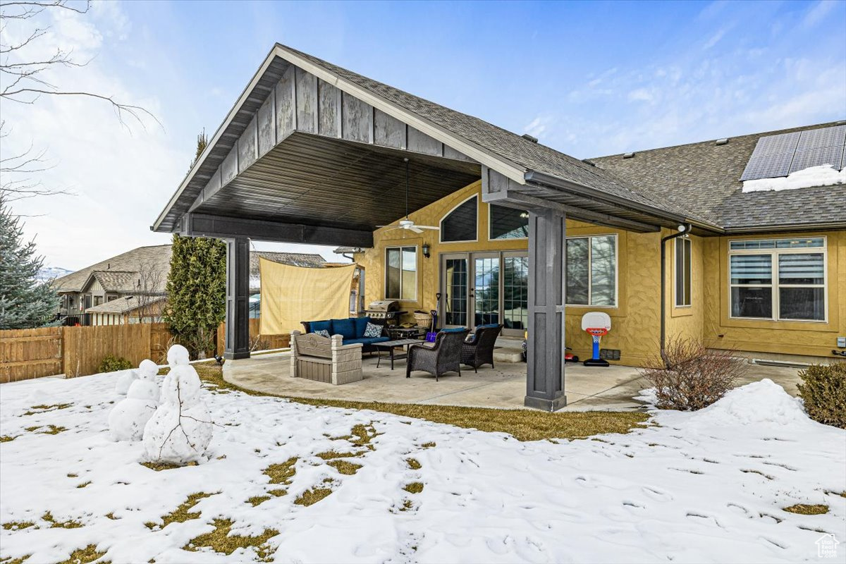 Snow covered back of property featuring a patio, an outdoor hangout area, roof with shingles, fence, and roof mounted solar panels