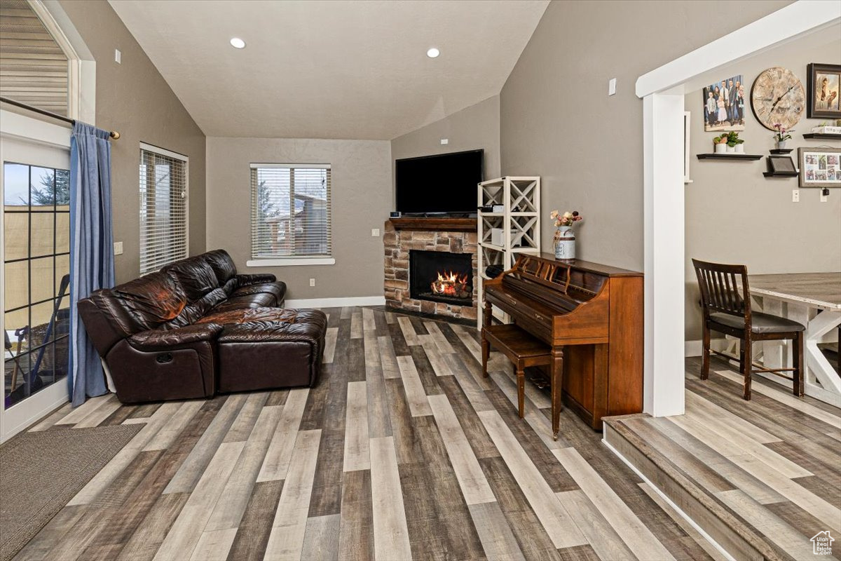 Living room with lofted ceiling, a stone fireplace, and hardwood / wood-style flooring