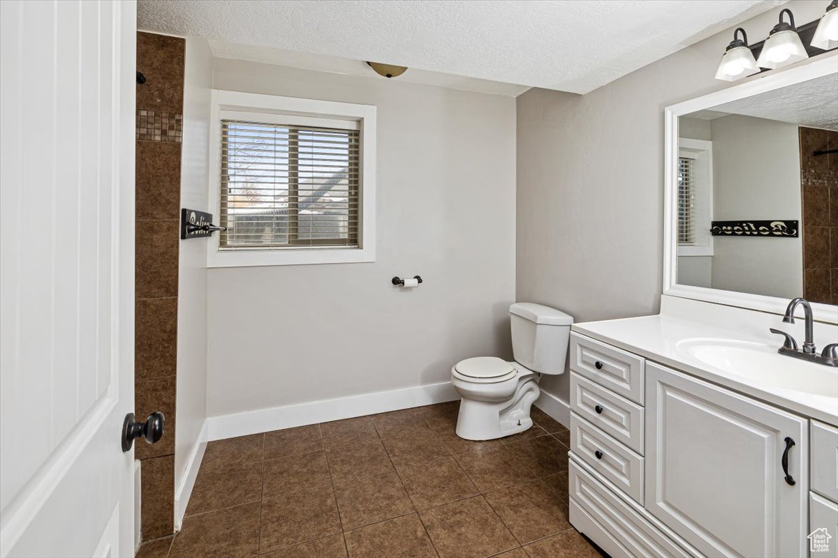 Bathroom featuring a textured ceiling, toilet, vanity, and tile patterned flooring