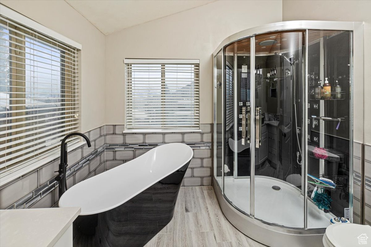 Bathroom featuring tile walls, hardwood / wood-style flooring, separate shower and tub, and lofted ceiling