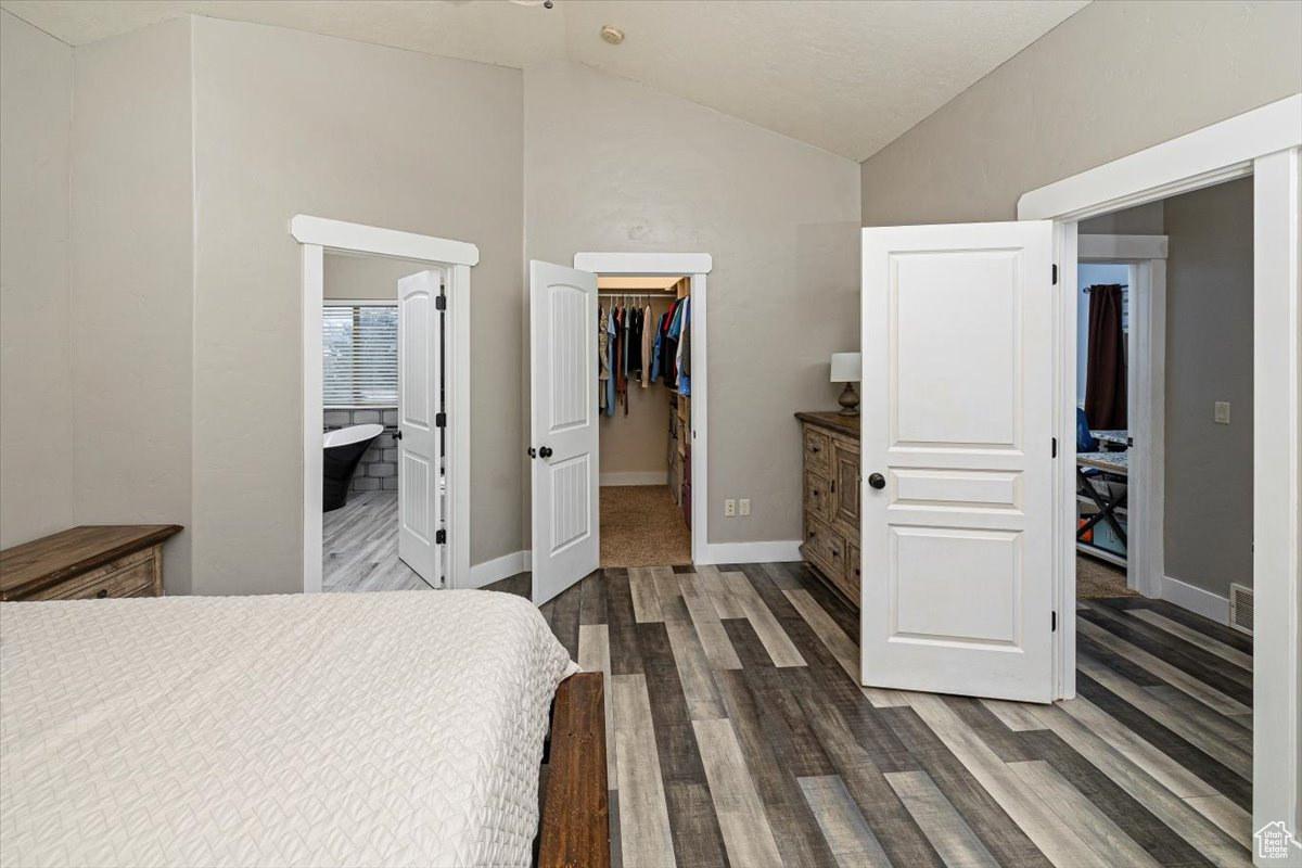 Bedroom featuring a closet, a spacious closet, dark wood-type flooring, vaulted ceiling, and ensuite bathroom