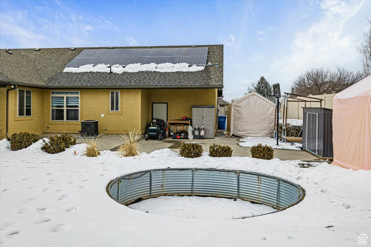 Snow covered rear of property featuring central air condition unit, roof with shingles, solar panels, and stucco siding