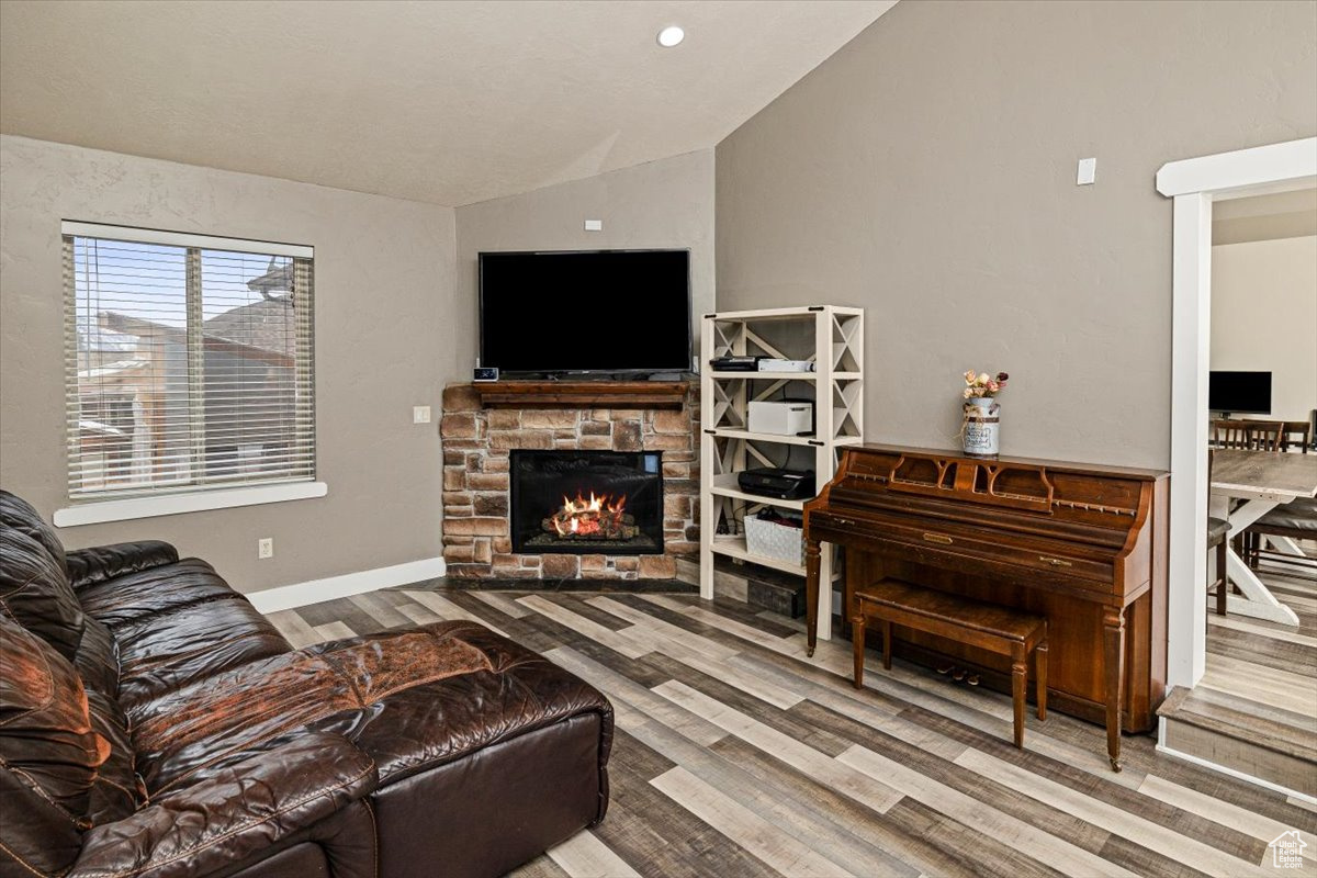 Living room featuring hardwood / wood-style flooring, lofted ceiling, and a stone fireplace