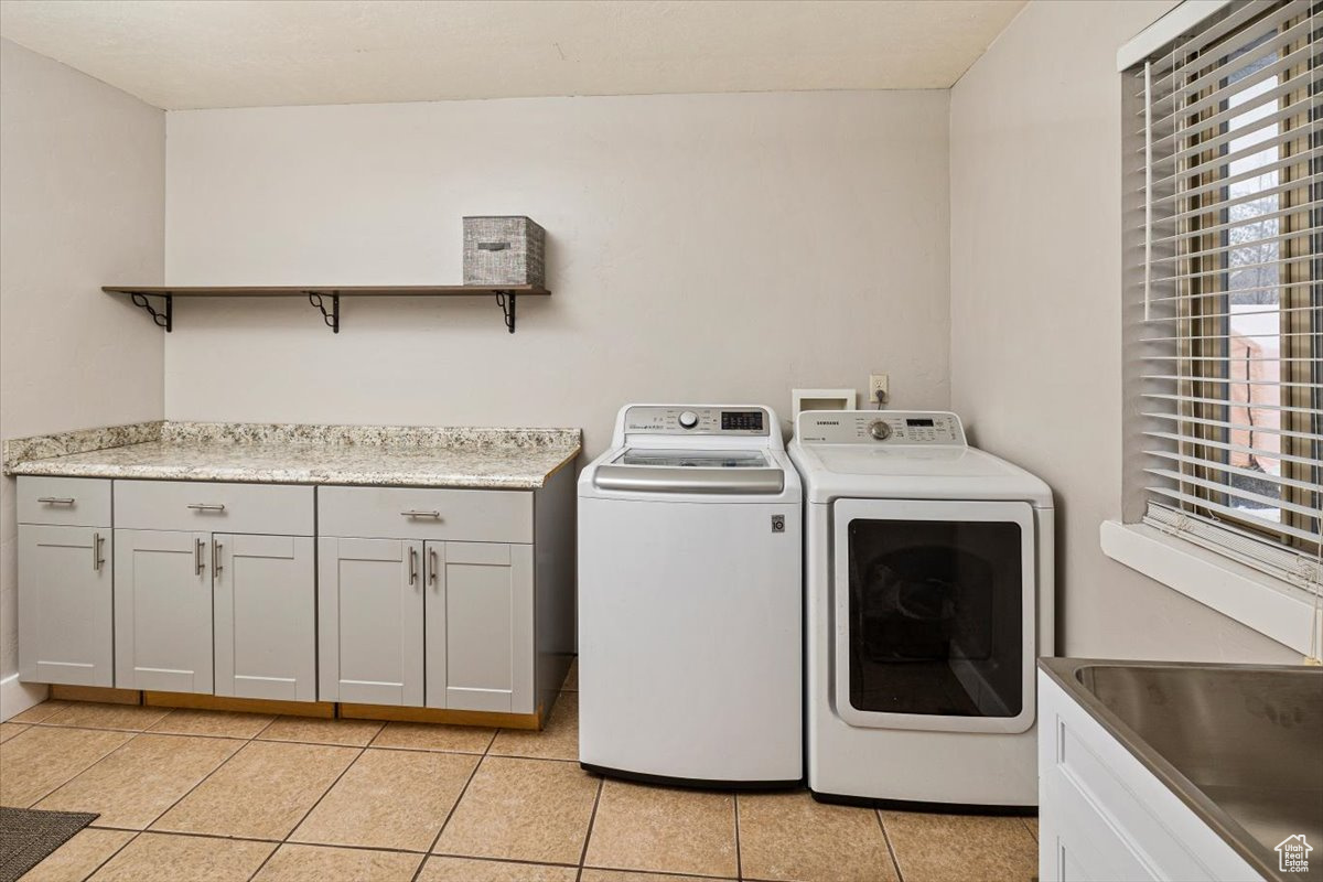 Washroom with sink, light tile patterned flooring, independent washer and dryer, and cabinets