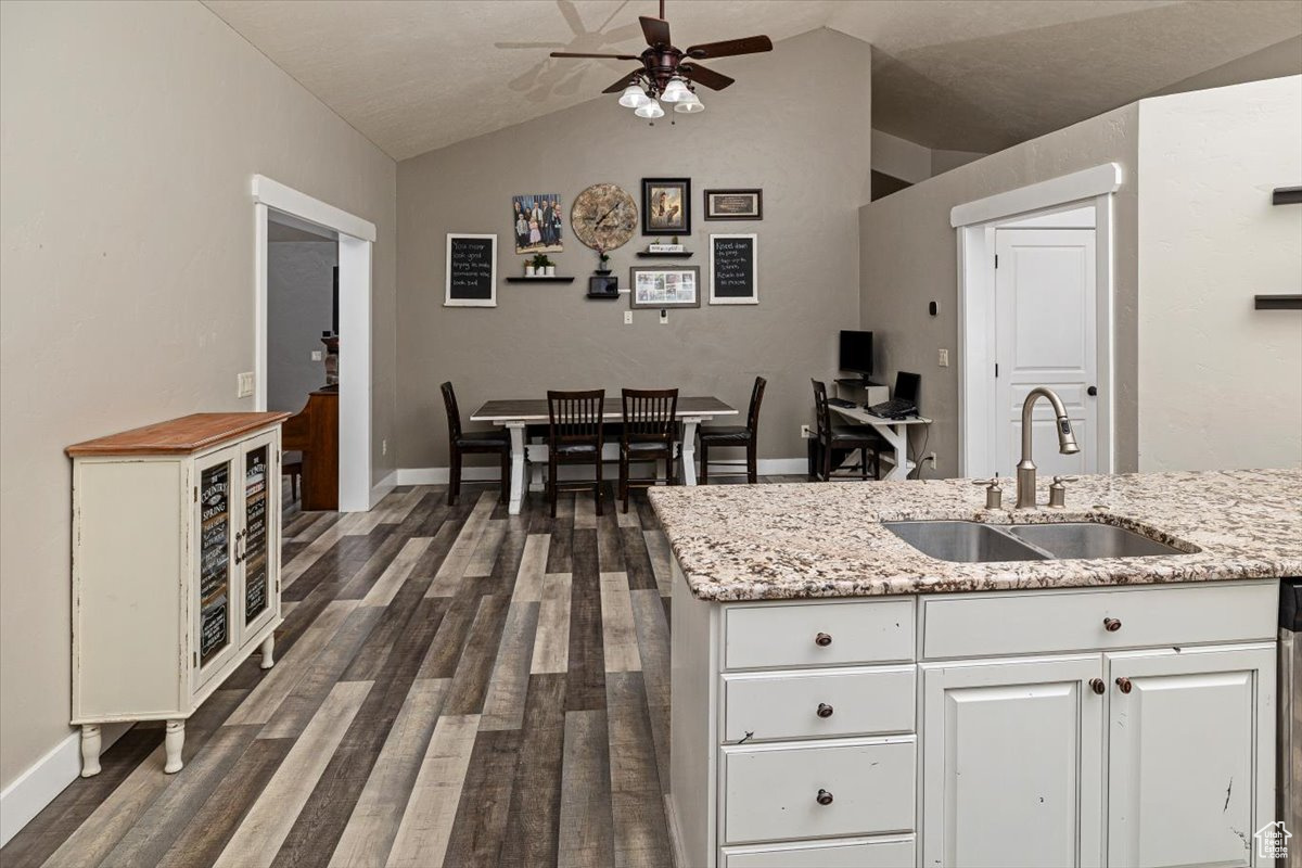 Kitchen with lofted ceiling, sink, light stone counters, white cabinetry, and dark hardwood / wood-style floors