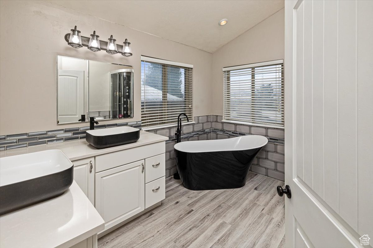 Bathroom featuring hardwood / wood-style flooring, lofted ceiling, a bath, tile walls, and vanity