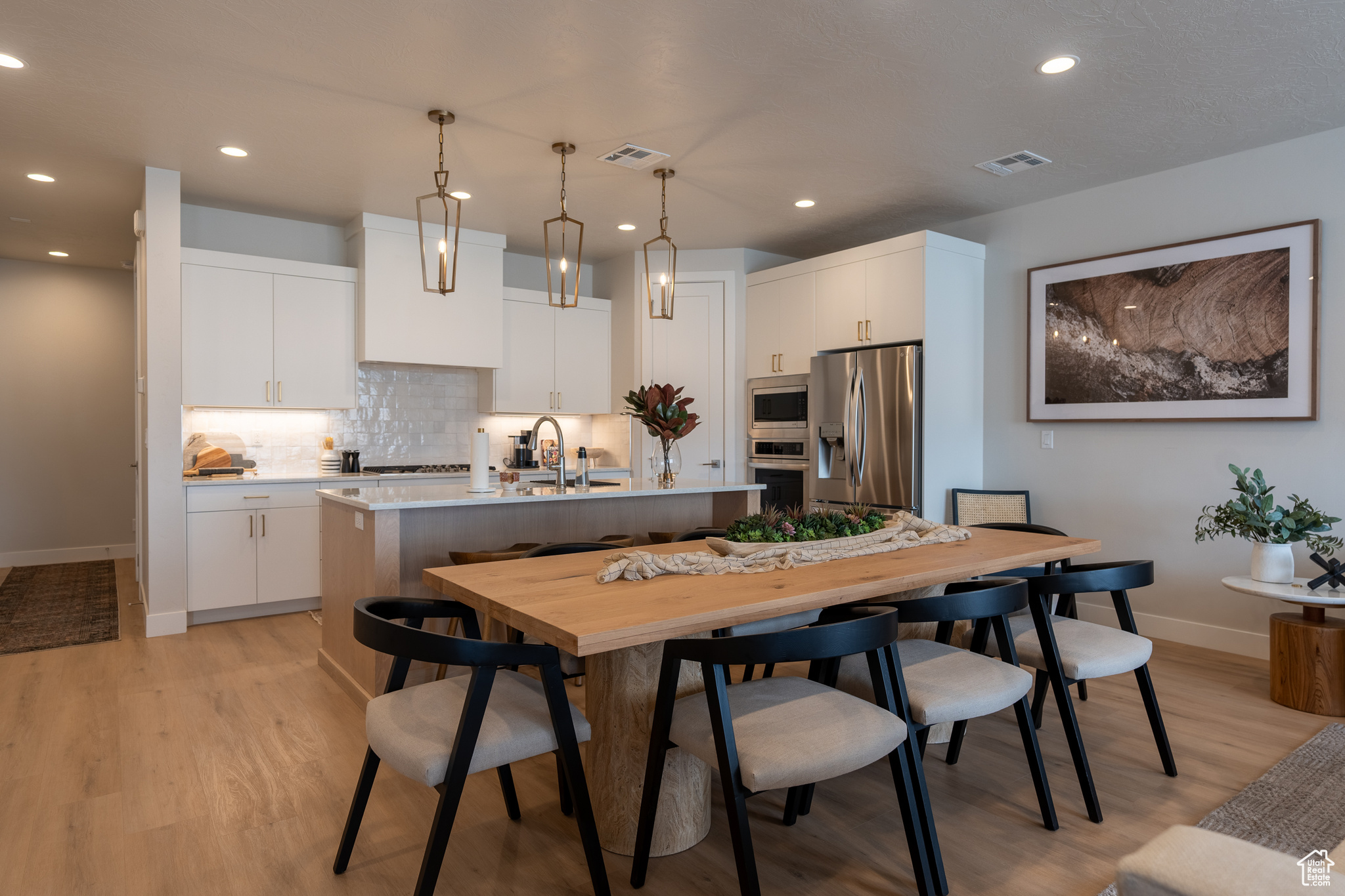Kitchen with appliances with stainless steel finishes, an island with sink, decorative backsplash, pendant lighting, and white cabinetry