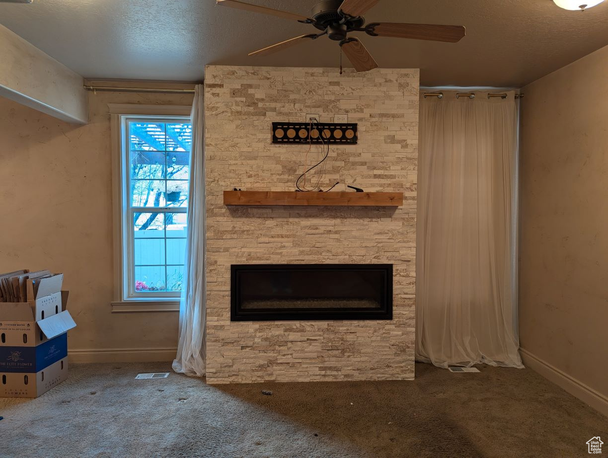 Unfurnished living room featuring a healthy amount of sunlight, carpet flooring, a textured ceiling, and a stone fireplace