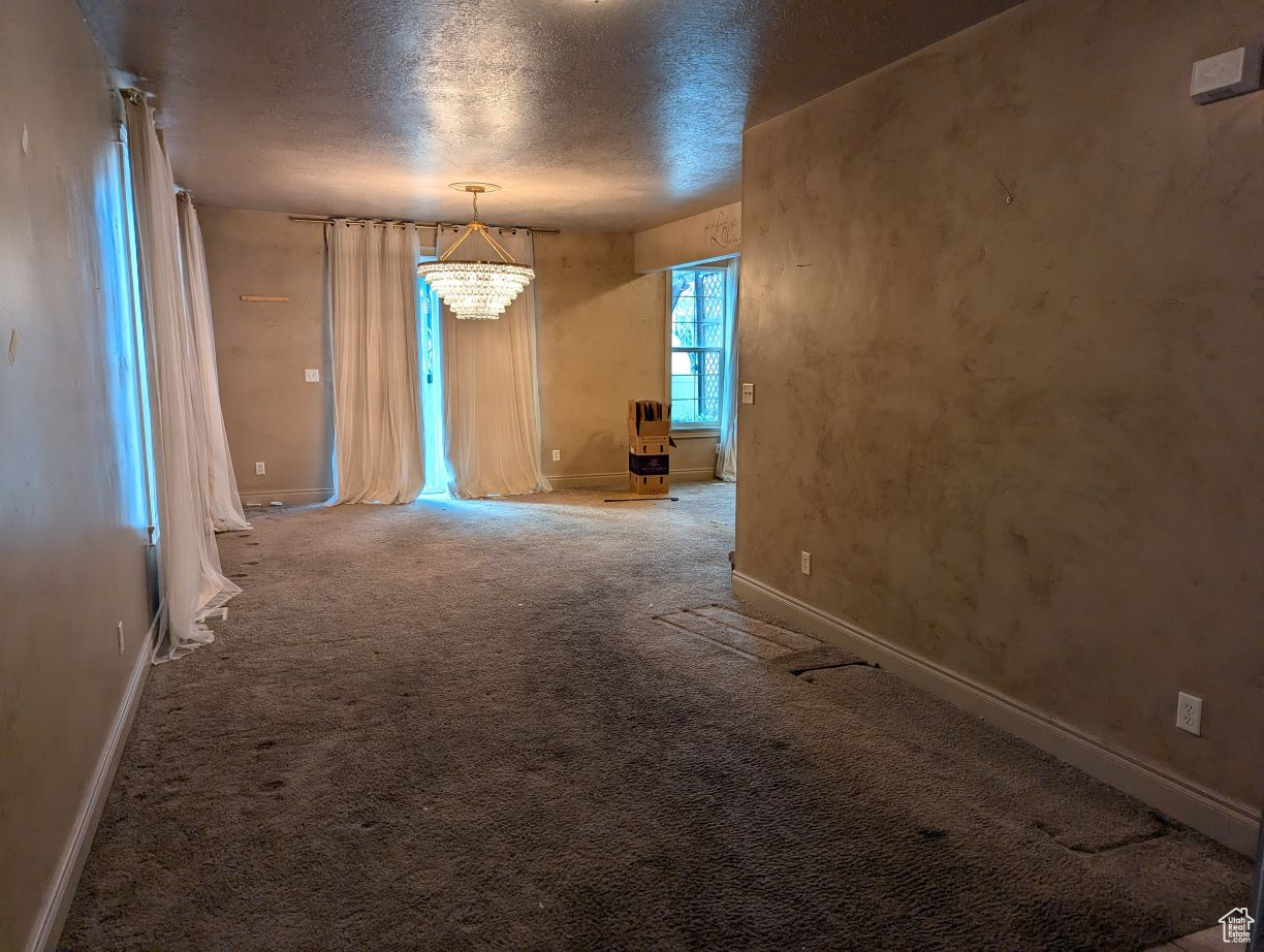 Unfurnished room featuring carpet floors, a textured ceiling, and an inviting chandelier