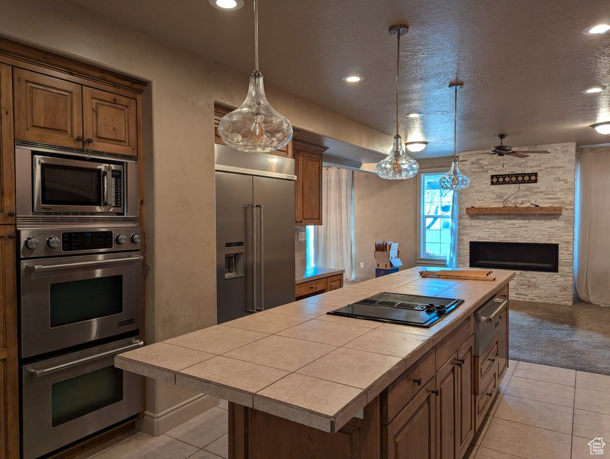 Kitchen with built in appliances, pendant lighting, a kitchen island, a textured ceiling, and tile countertops