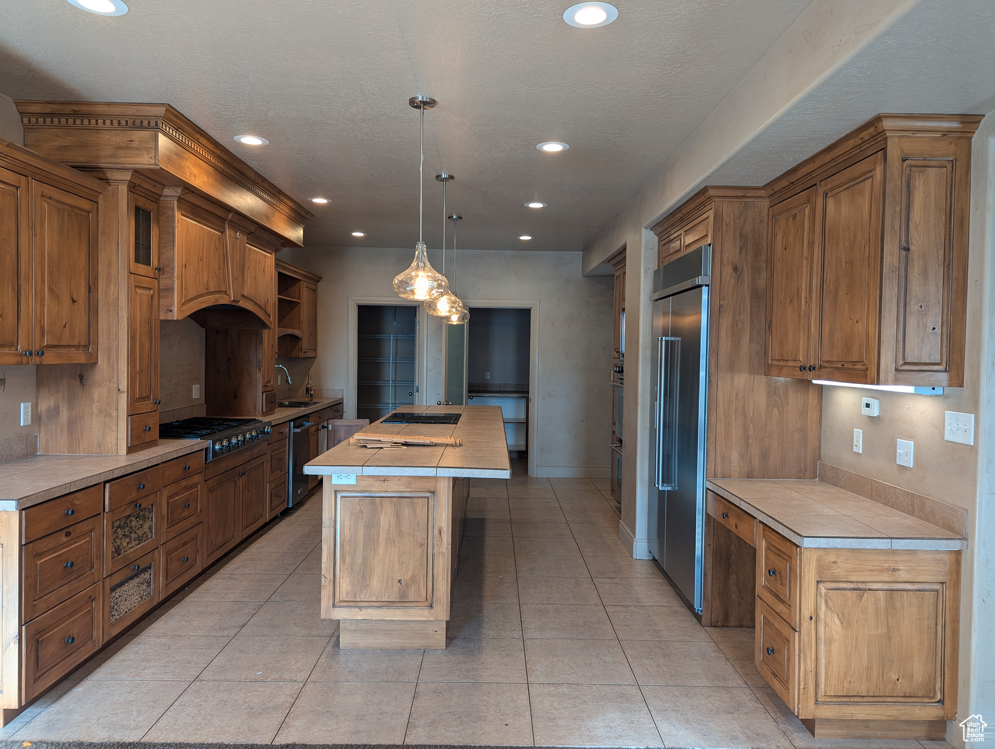 Kitchen with light tile patterned floors, sink, appliances with stainless steel finishes, pendant lighting, and a kitchen island