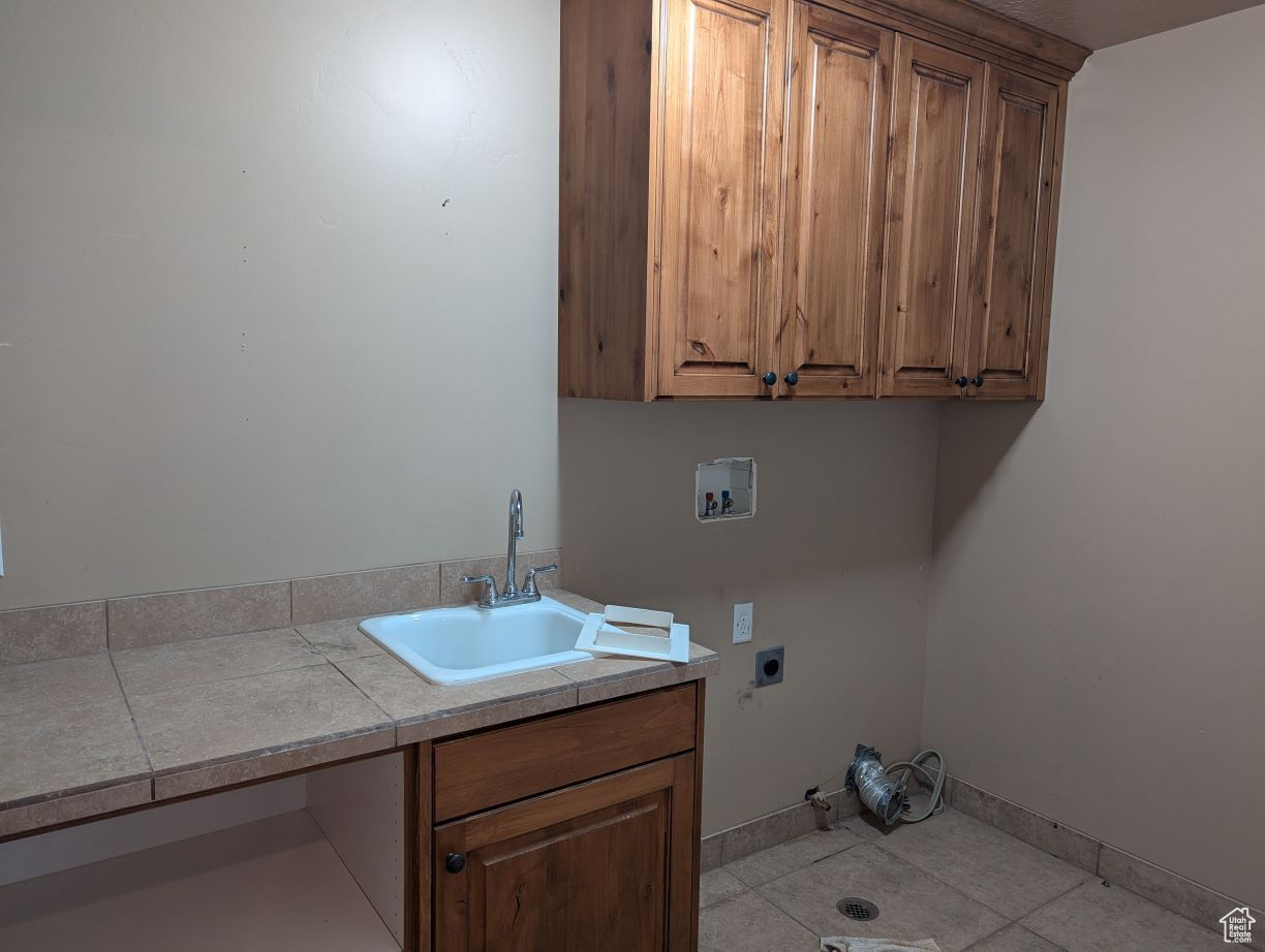 Laundry room with cabinets, hookup for an electric dryer, hookup for a washing machine, sink, and light tile patterned floors
