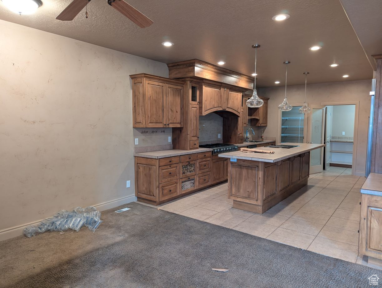 Kitchen featuring hanging light fixtures, custom range hood, stainless steel gas cooktop, a kitchen island, and light colored carpet