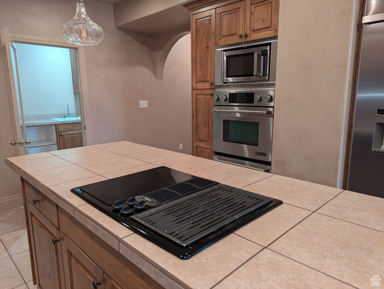 Kitchen featuring appliances with stainless steel finishes, light tile patterned floors, sink, hanging light fixtures, and tile counters