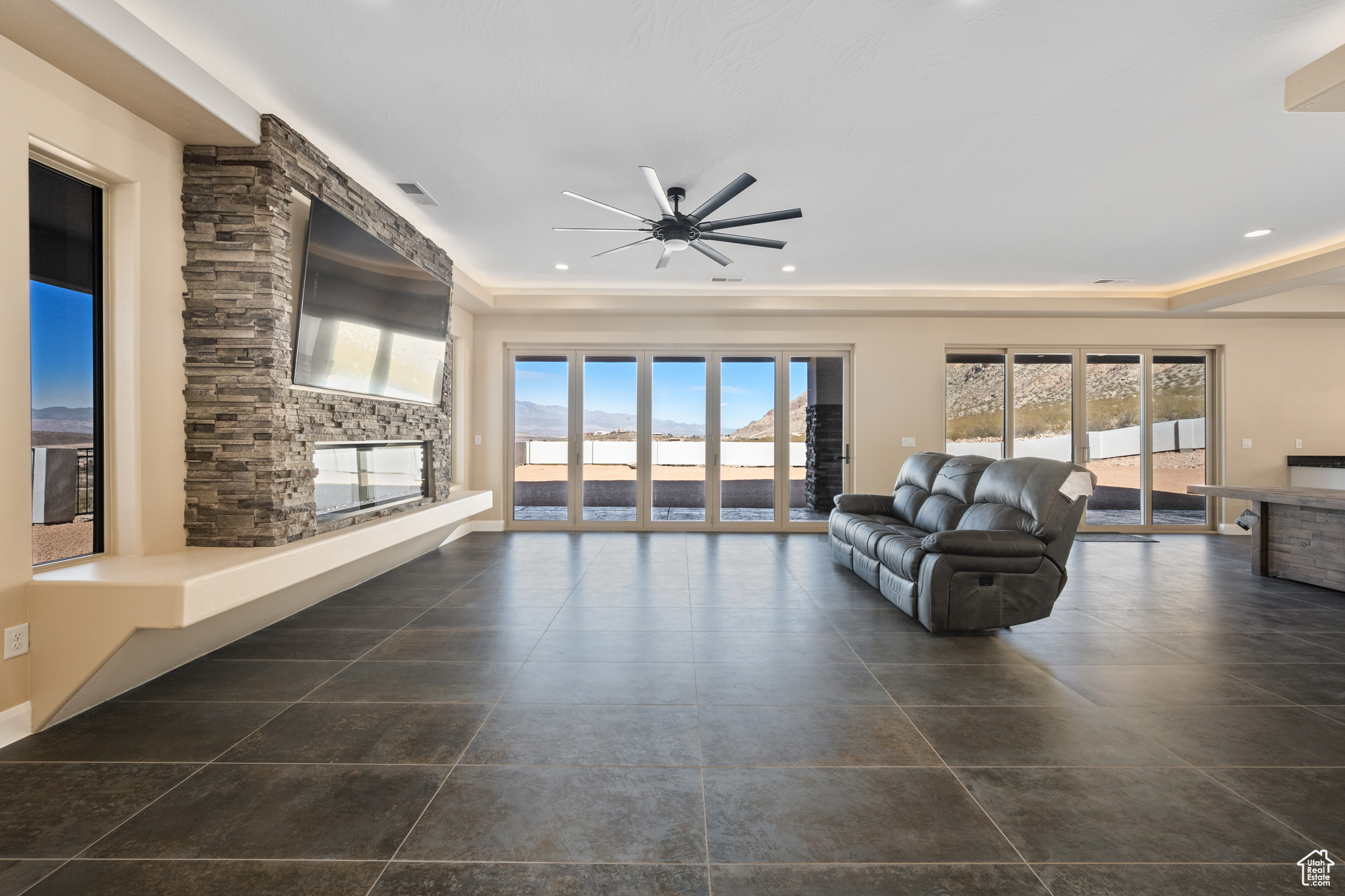 Living room featuring ceiling fan, a stone fireplace, and a wealth of natural light
