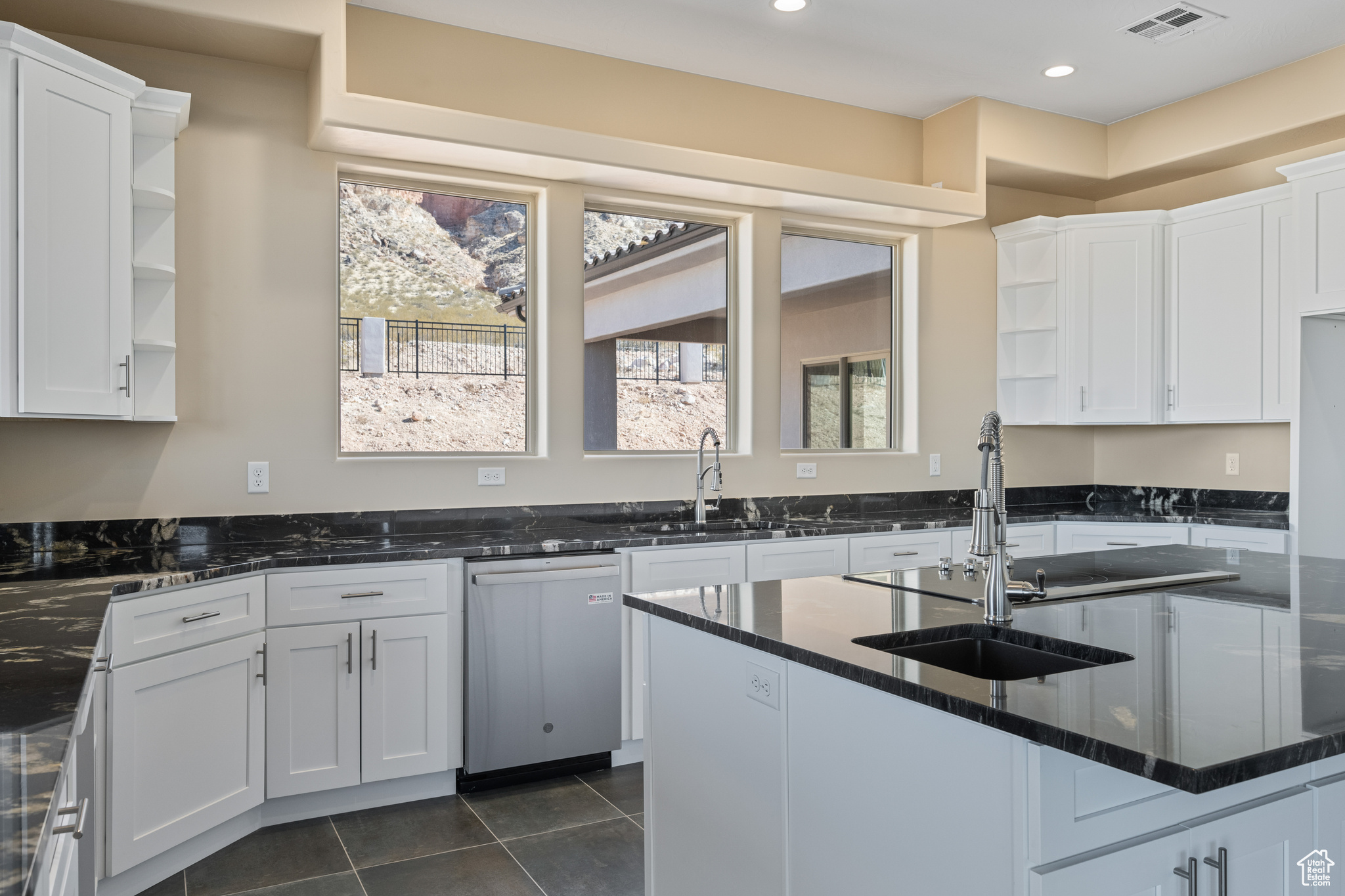 Kitchen featuring white cabinetry, sink, stainless steel dishwasher, and dark stone counters