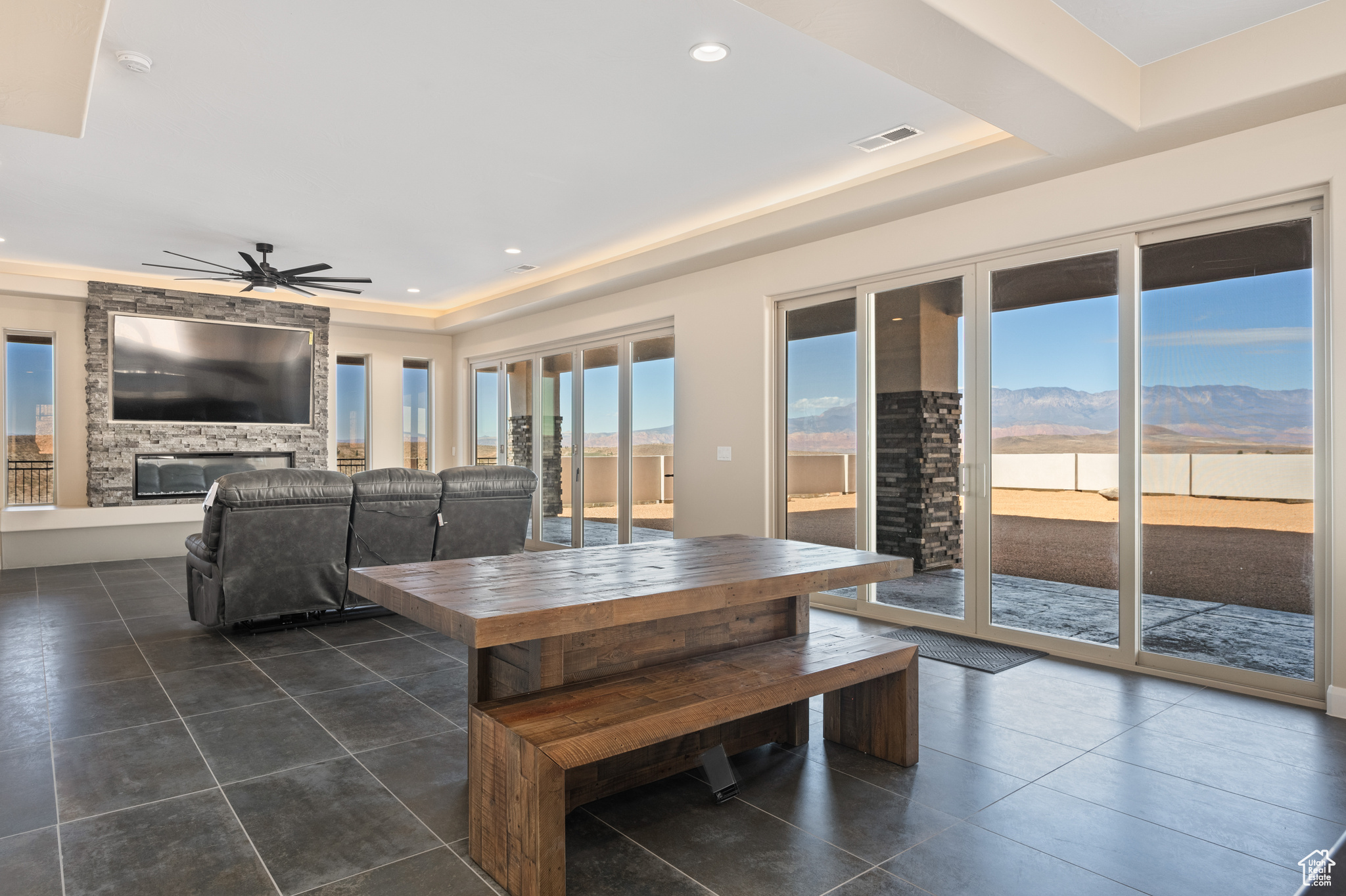 Unfurnished dining area featuring ceiling fan, a stone fireplace, a raised ceiling, and dark tile patterned flooring