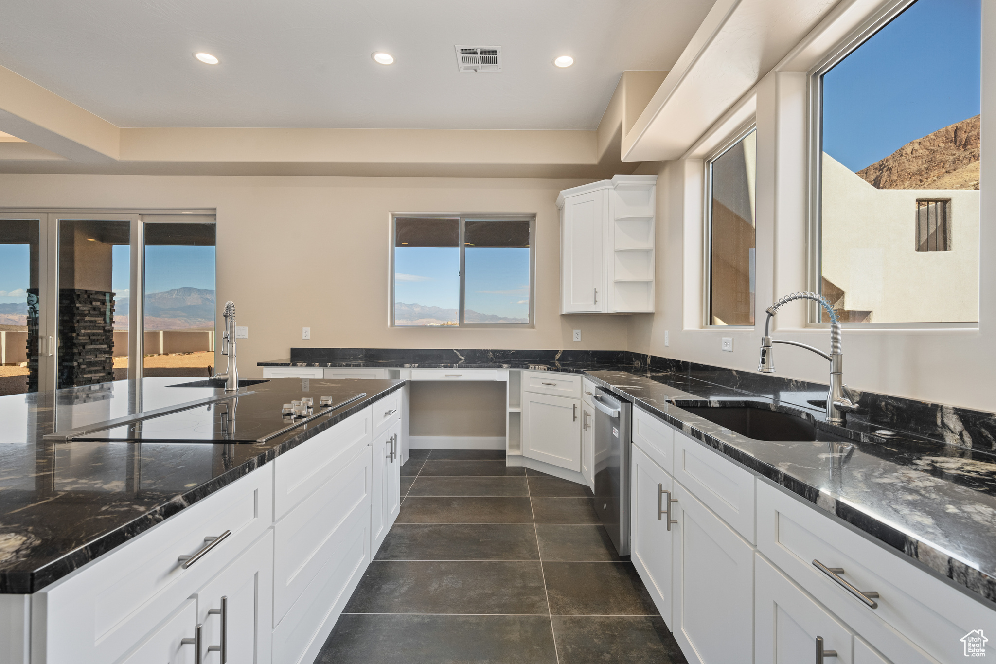 Kitchen with sink, dishwasher, white cabinetry, dark stone countertops, and black electric stovetop