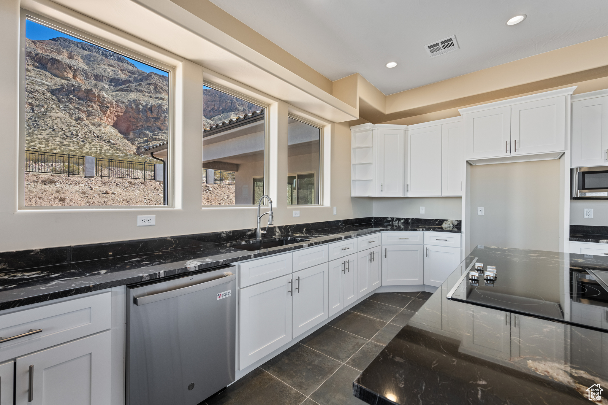 Kitchen with white cabinetry, appliances with stainless steel finishes, sink, and dark stone counters