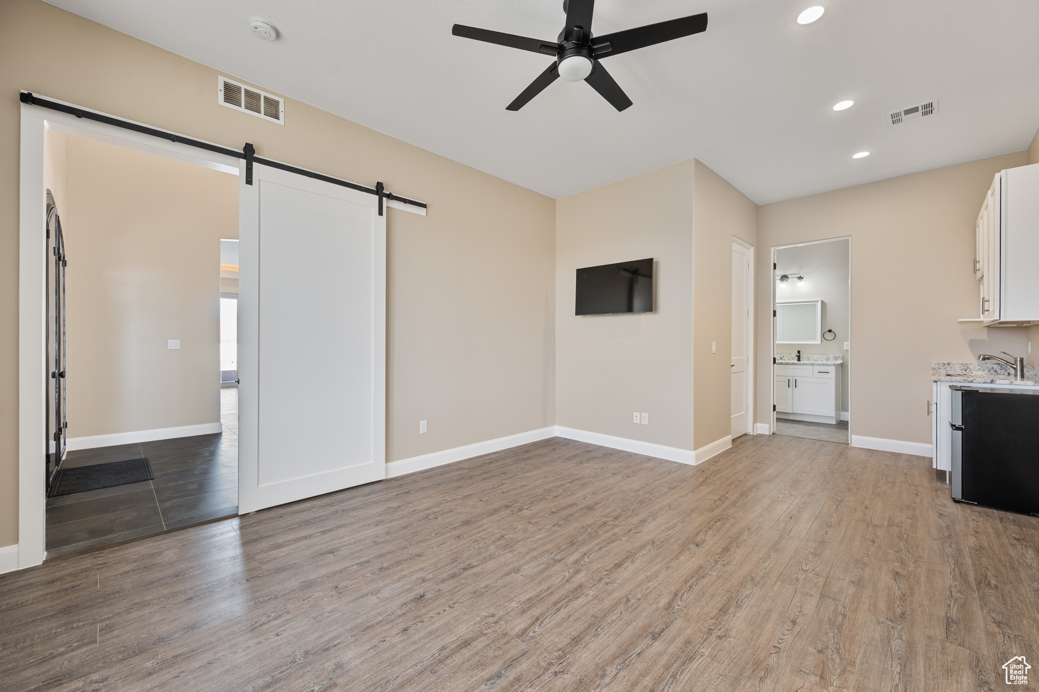 Unfurnished living room with light hardwood / wood-style flooring, a barn door, and ceiling fan
