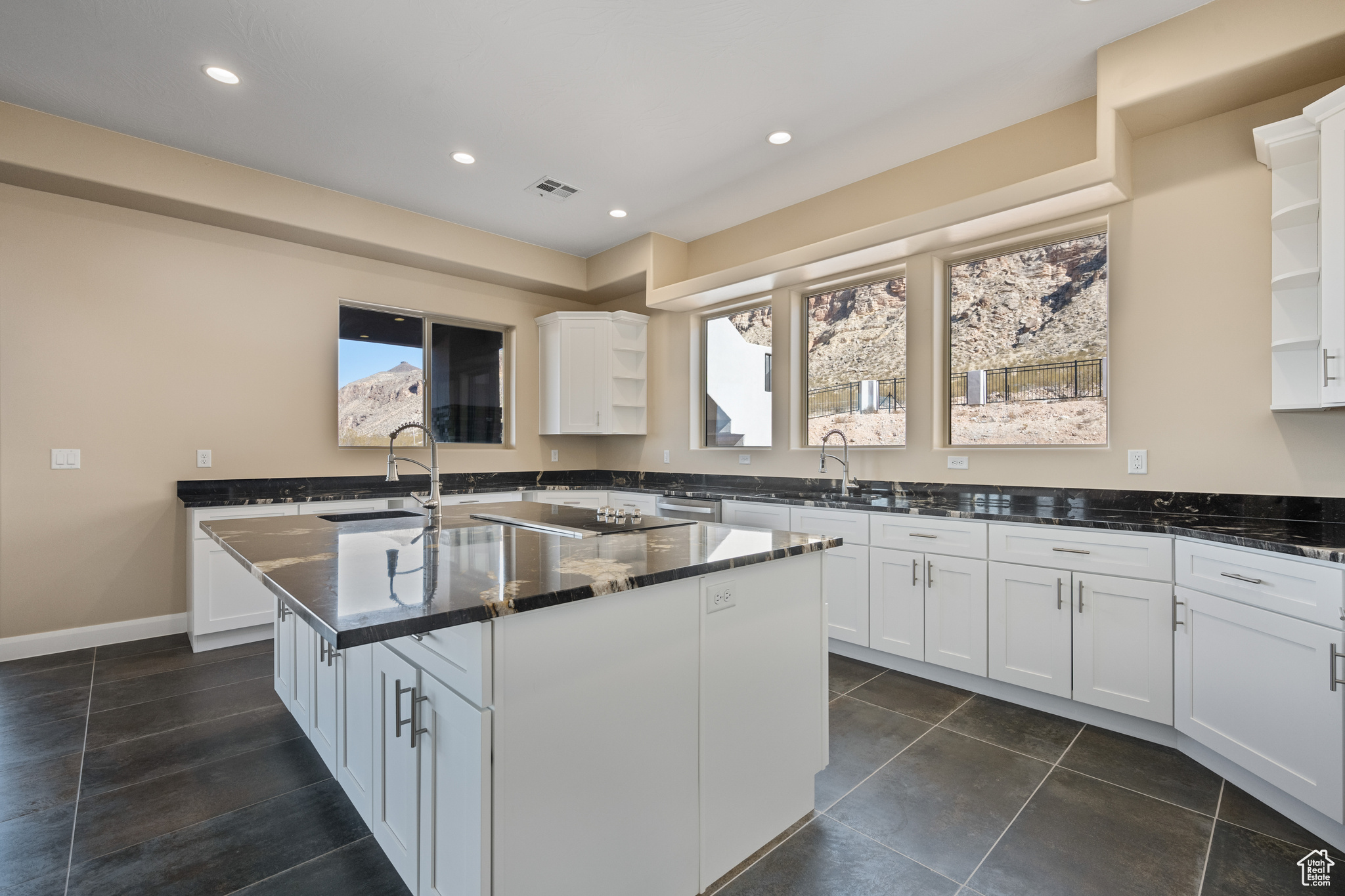 Kitchen with a kitchen island with sink, sink, white cabinets, and dark stone counters