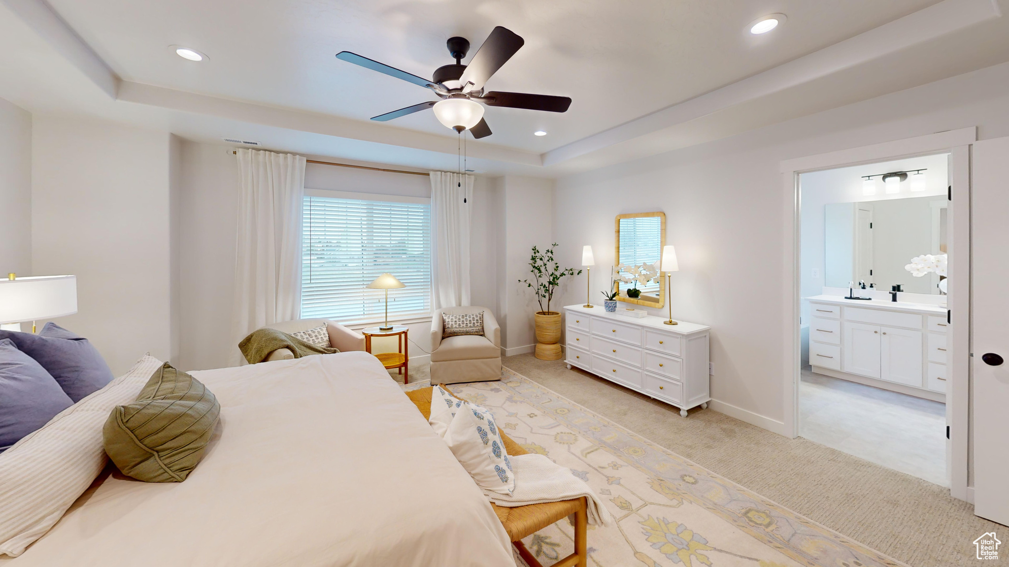 Carpeted bedroom with ceiling fan, ensuite bath, a tray ceiling, and sink