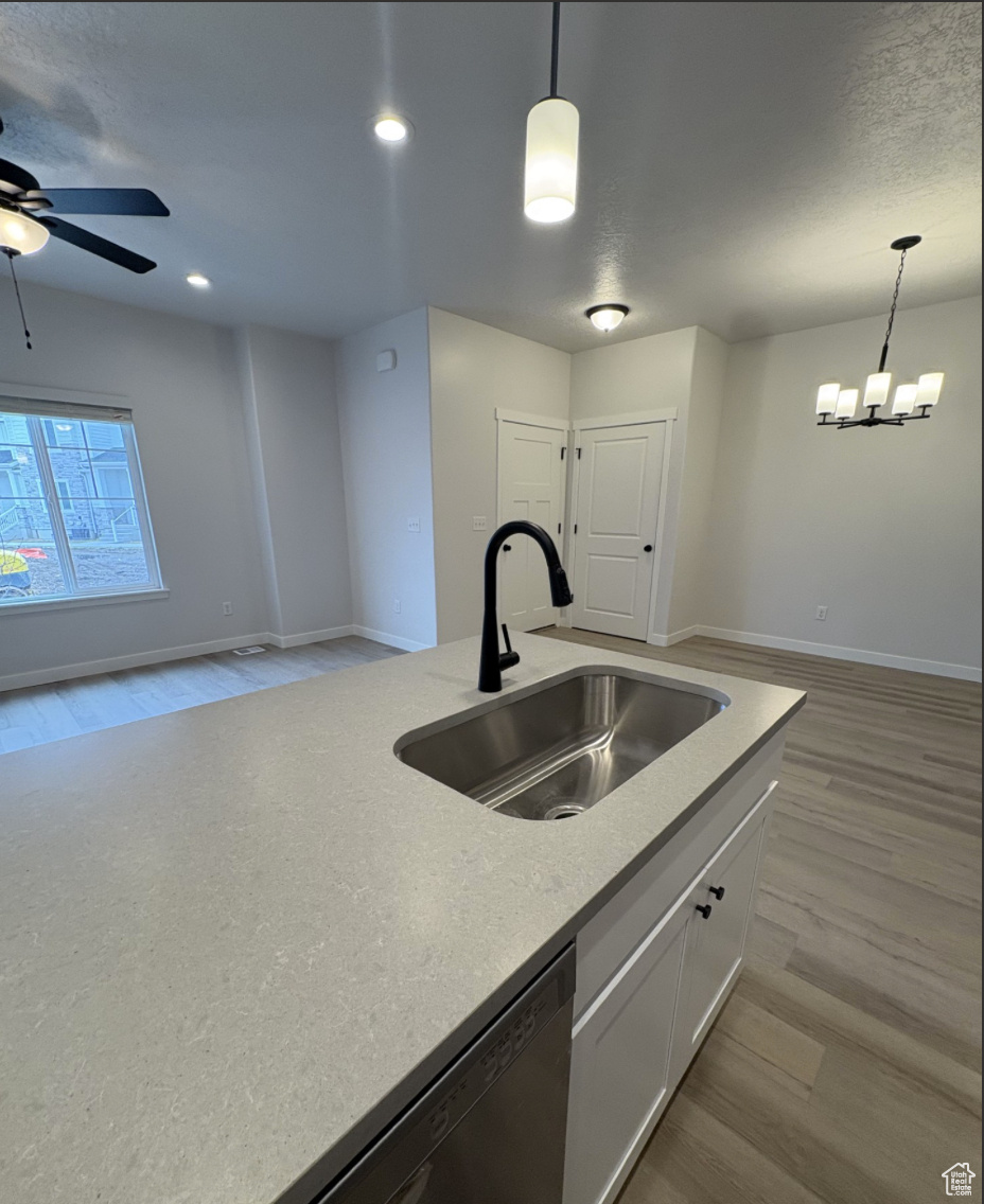 Kitchen featuring sink, light wood-type flooring, decorative light fixtures, ceiling fan with notable chandelier, and white cabinets