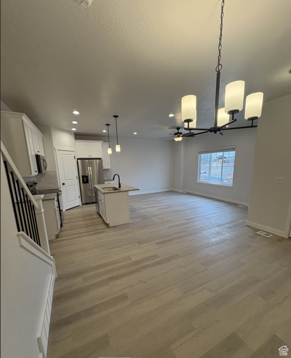 Kitchen with a center island with sink, sink, pendant lighting, stainless steel fridge with ice dispenser, and white cabinets