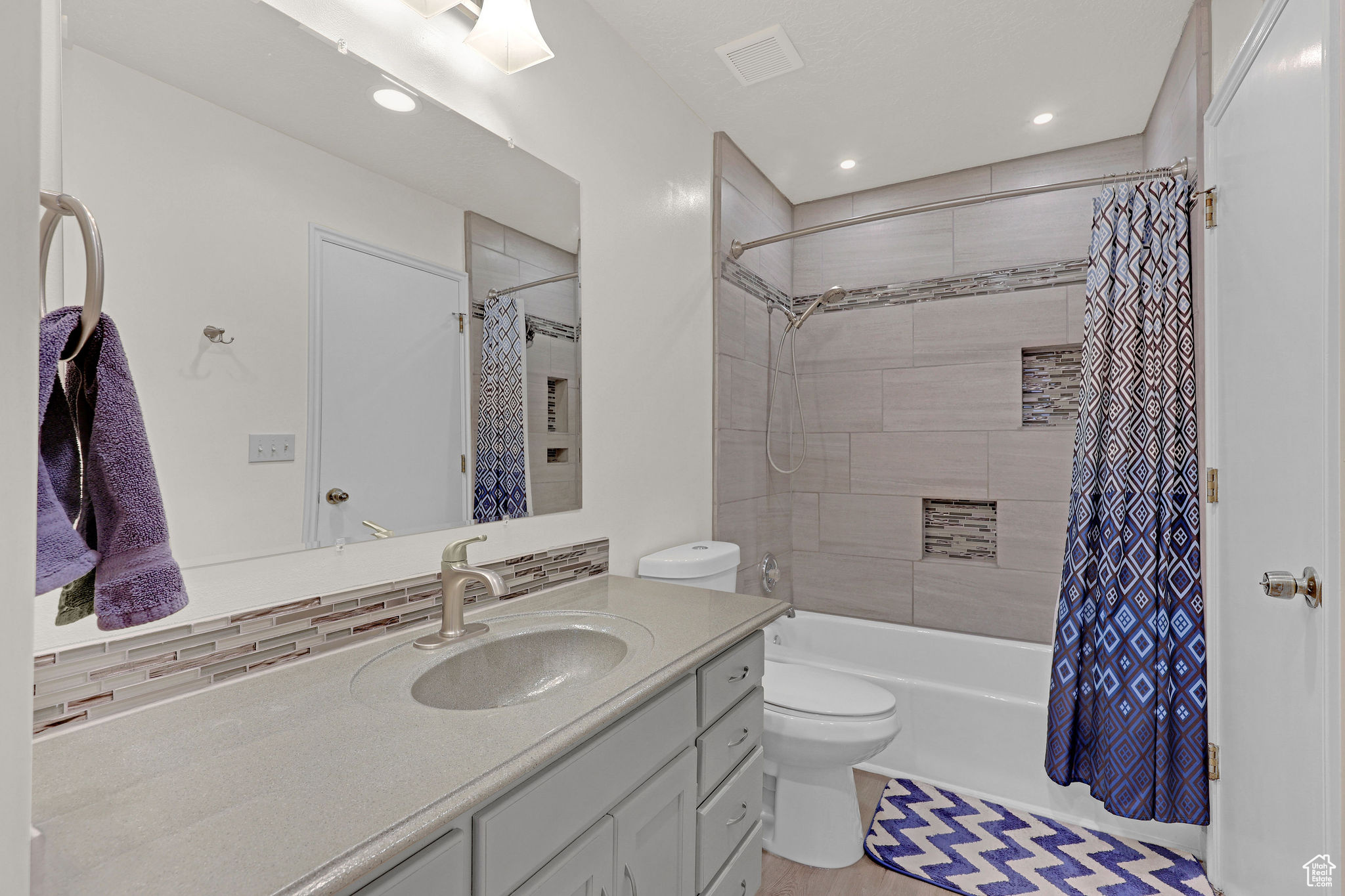 Full bathroom featuring shower / tub combo, toilet, vanity, and backsplash