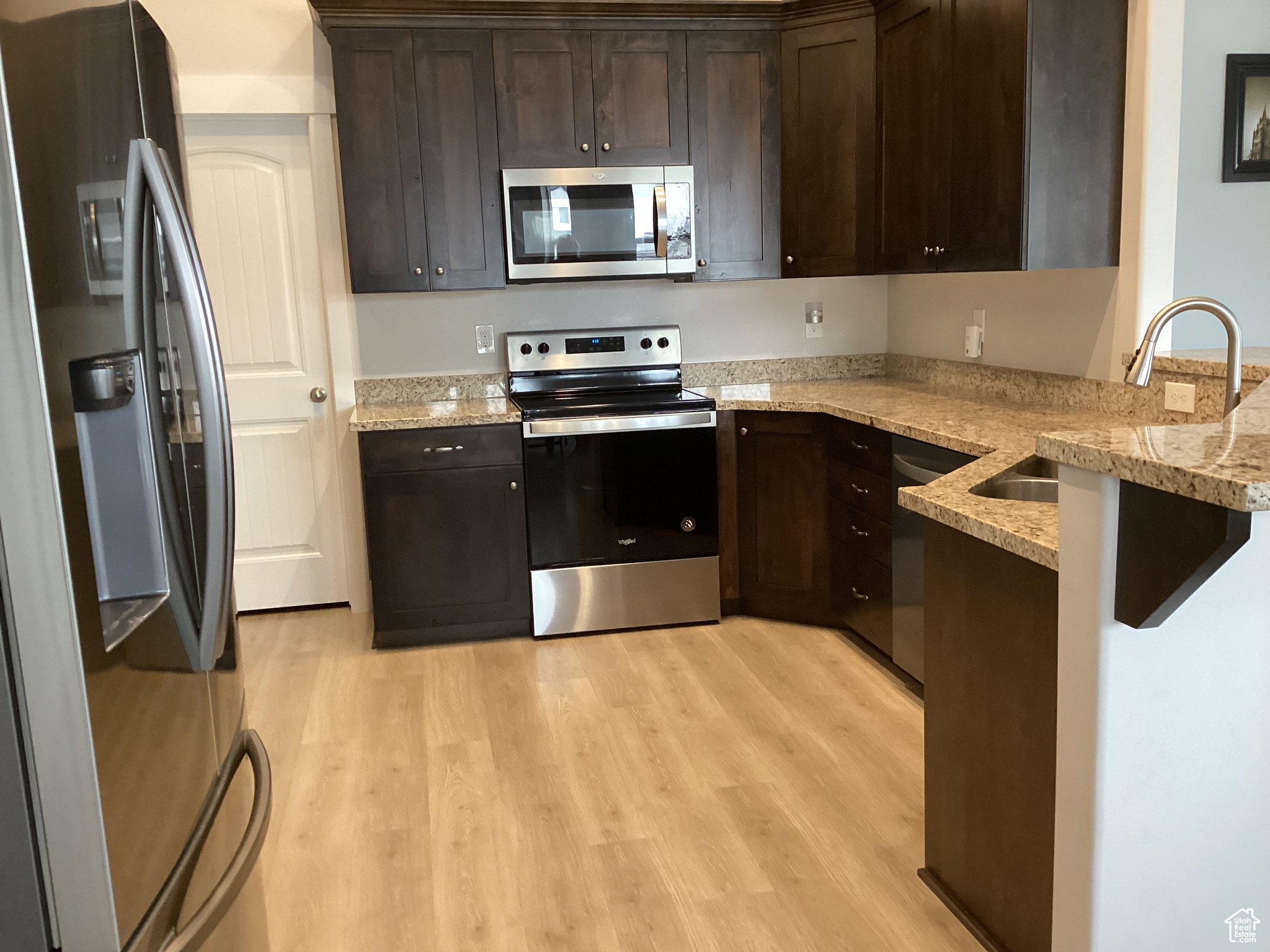 Kitchen featuring appliances with stainless steel finishes, sink, dark brown cabinets, and light stone countertops