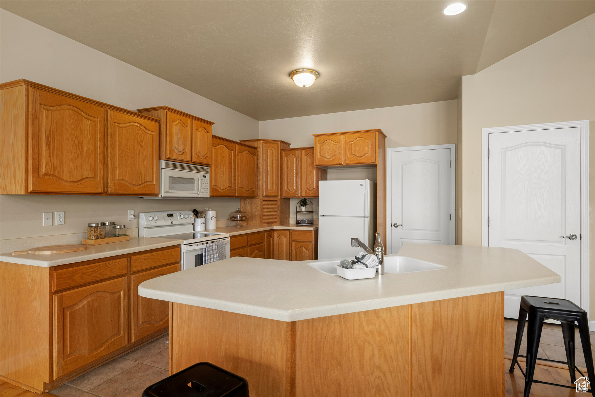 Kitchen with white appliances, an island with sink, light tile patterned floors, sink, and a kitchen bar