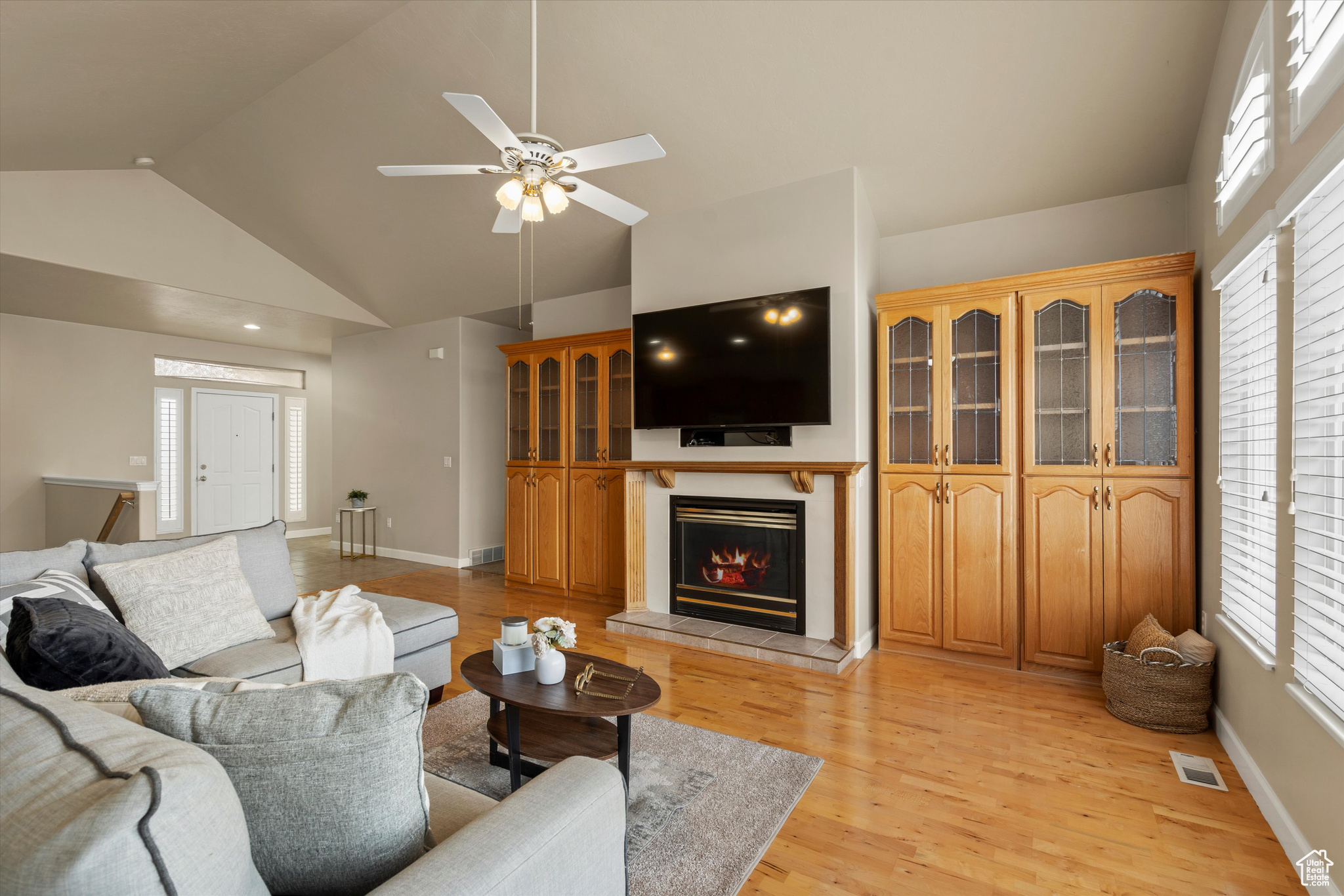 Living room featuring light wood-type flooring, a cozy fireplace, high vaulted ceiling, and ceiling fan