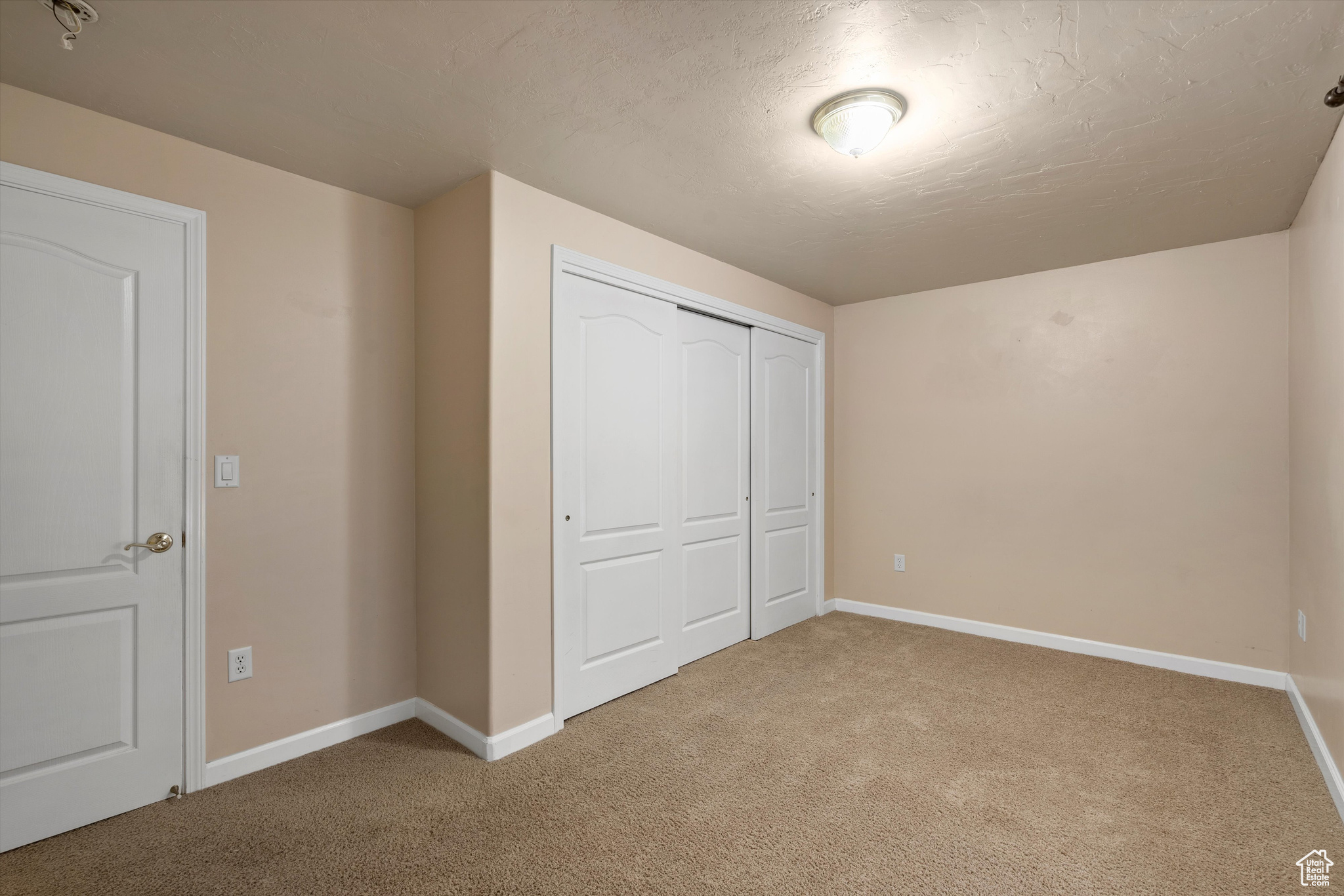 Unfurnished bedroom featuring a textured ceiling, light carpet, and a closet