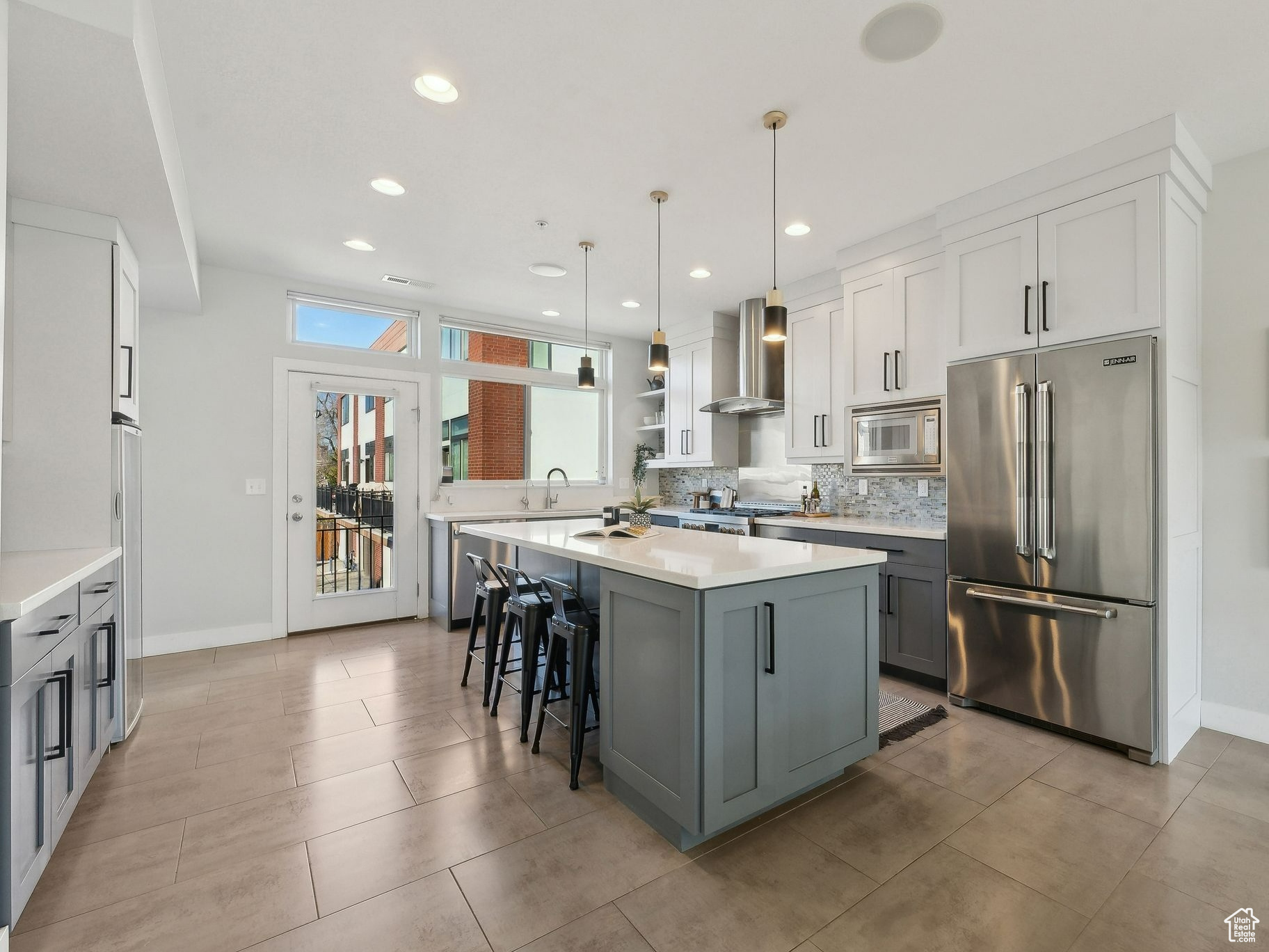 Kitchen with appliances with stainless steel finishes, gray cabinetry, hanging light fixtures, a center island, and wall chimney range hood