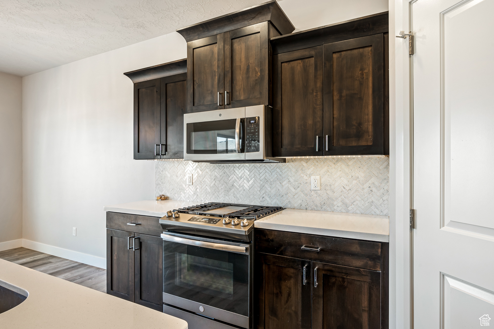 Kitchen with hardwood / wood-style flooring, stainless steel appliances, dark brown cabinetry, tasteful backsplash, and a textured ceiling