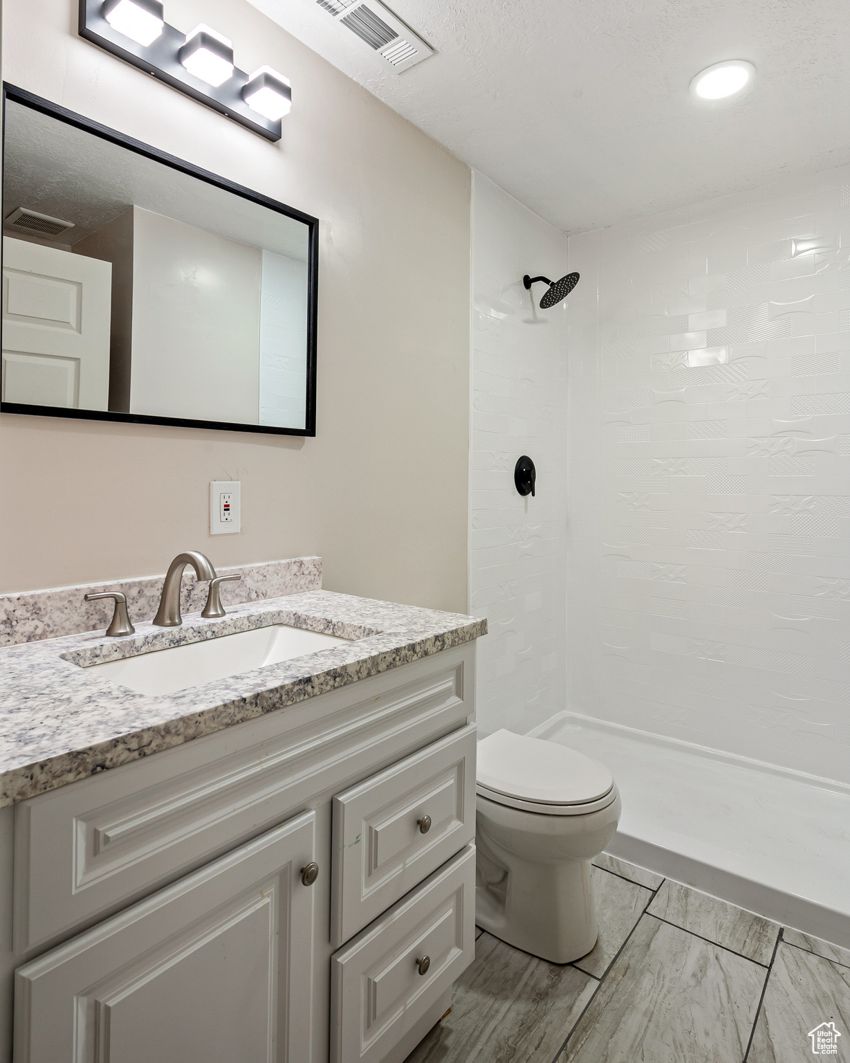 Bathroom with vanity, tiled shower, and toilet