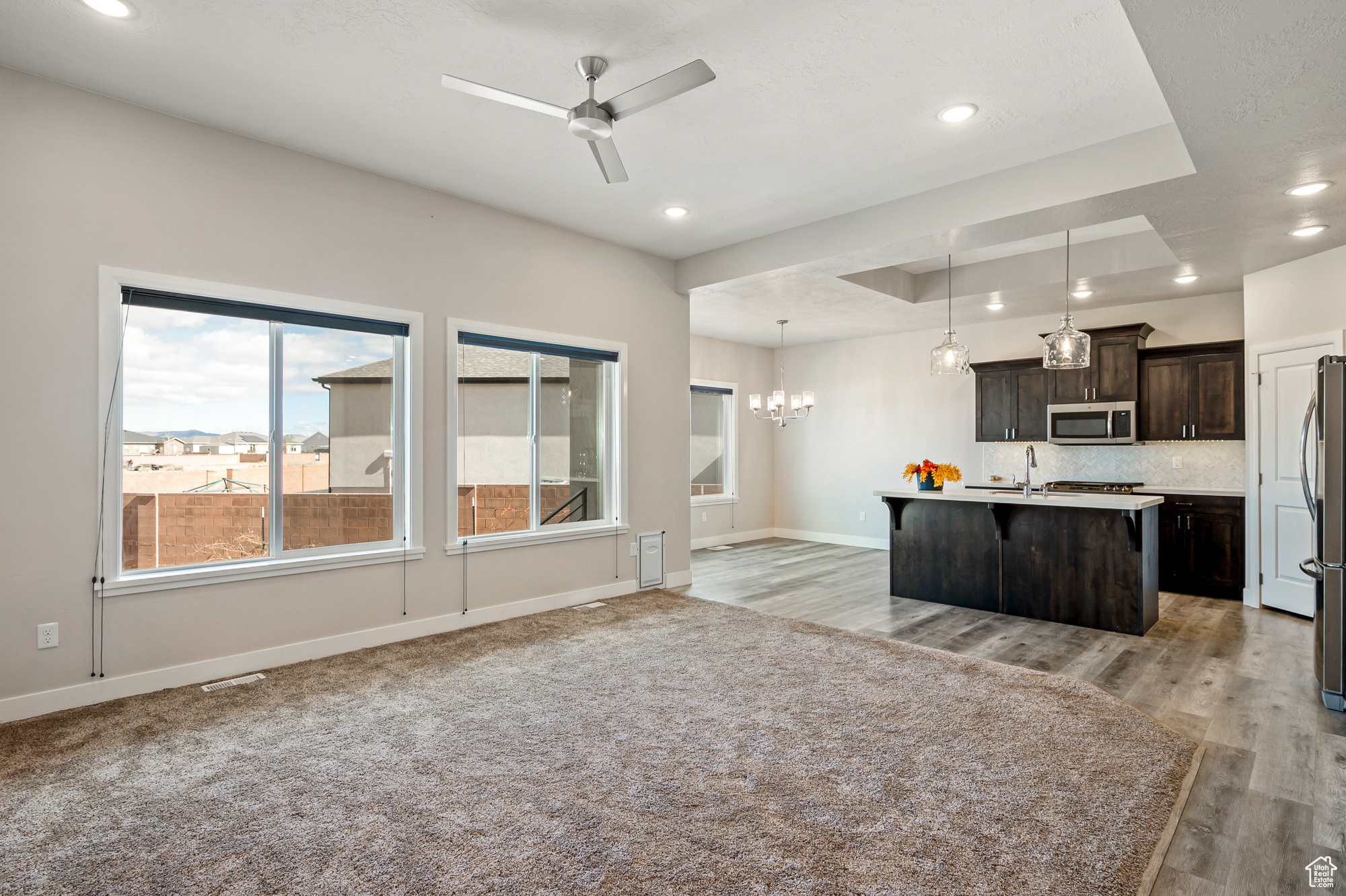 Kitchen with appliances with stainless steel finishes, a tray ceiling, decorative light fixtures, an island with sink, and dark brown cabinetry
